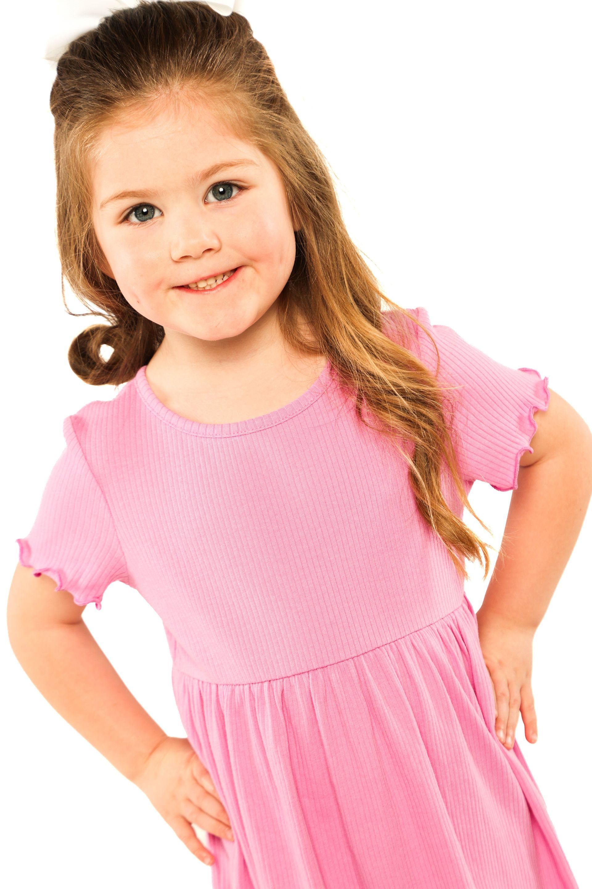 Young child in a pink dress smiling with hands on hips against a white background