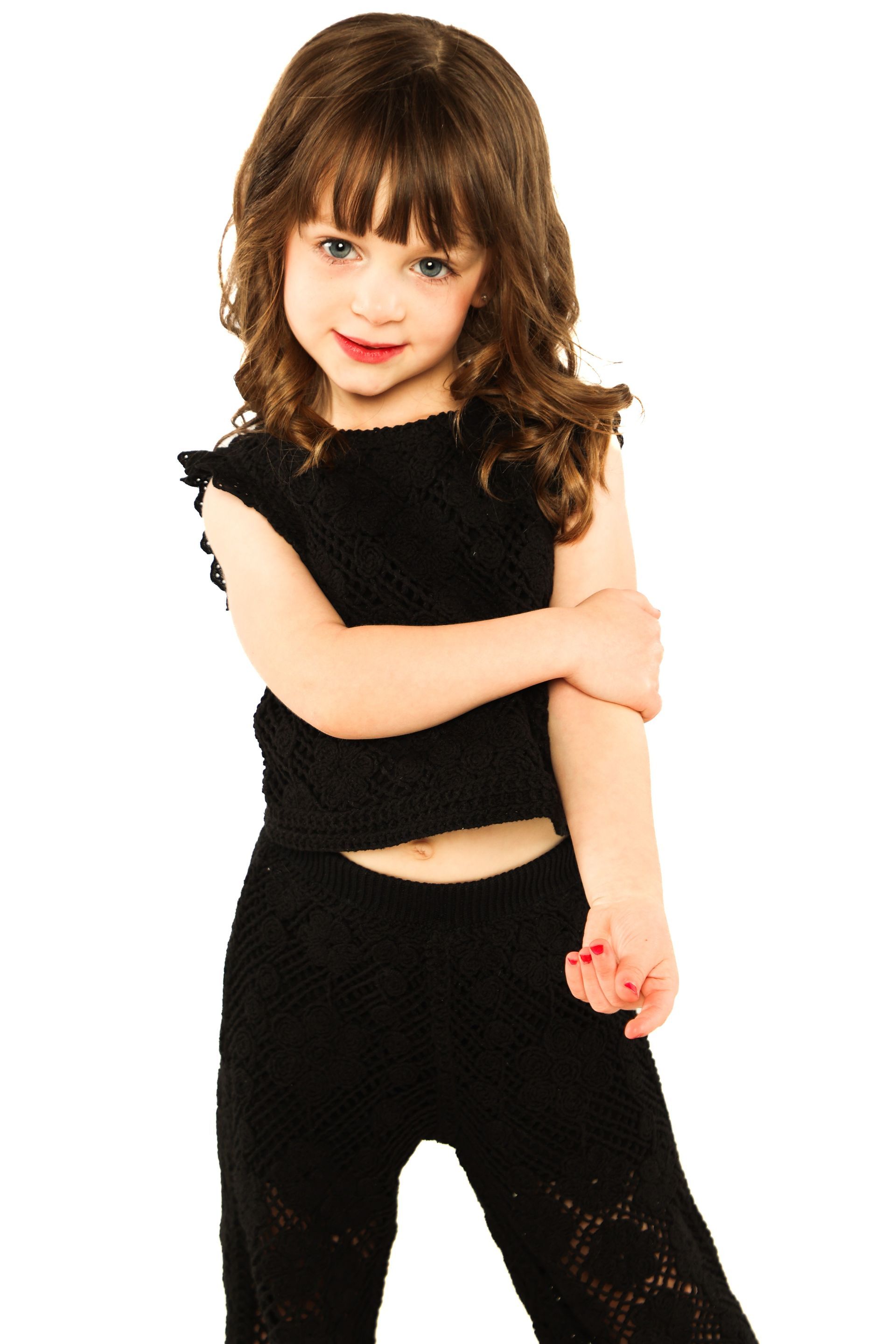 Young child in black outfit standing with arms crossed against a white background