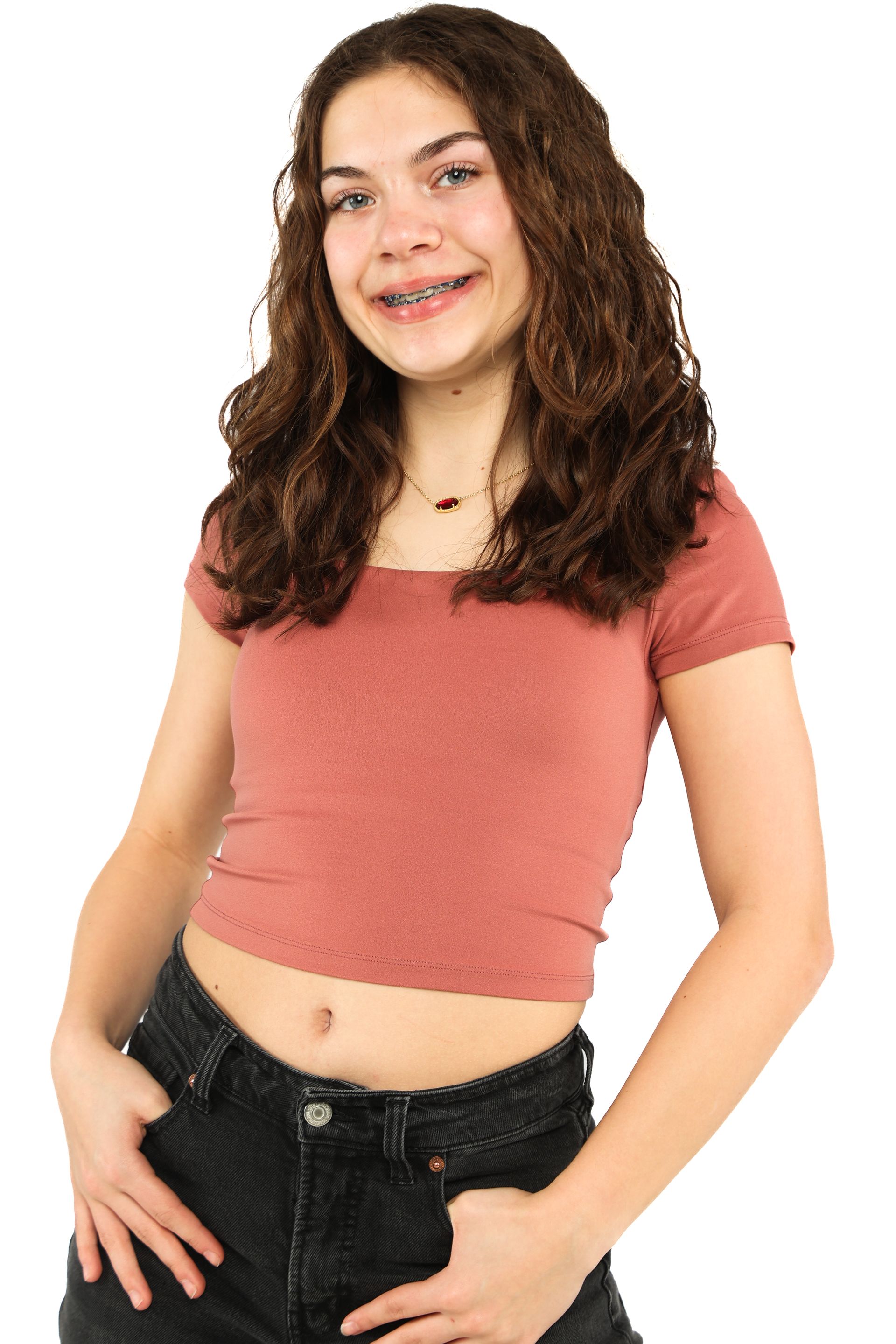 Young person in a pink crop top and black jeans, smiling against a white background