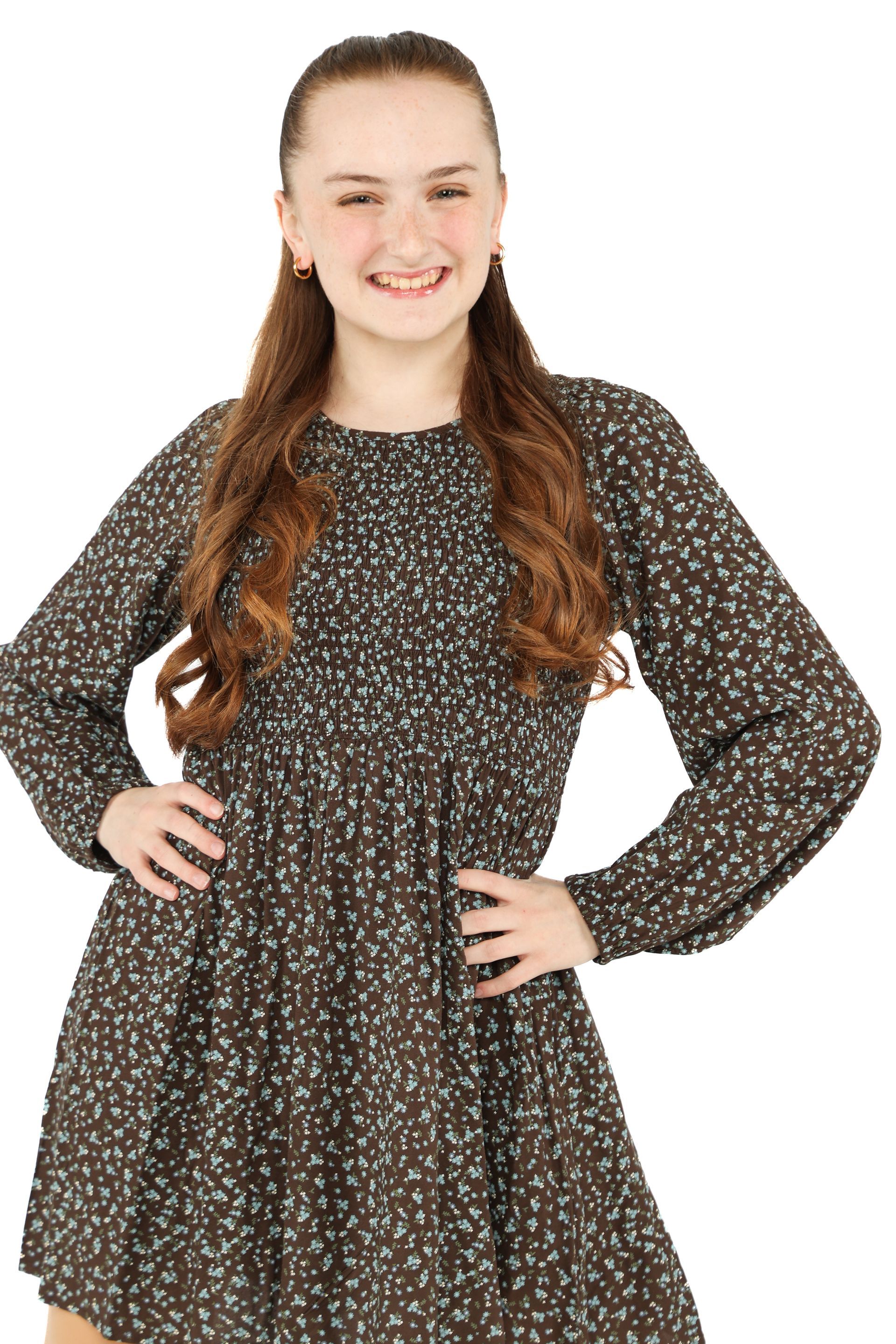 Woman standing with hands on hips, wearing a dark patterned dress against a white background