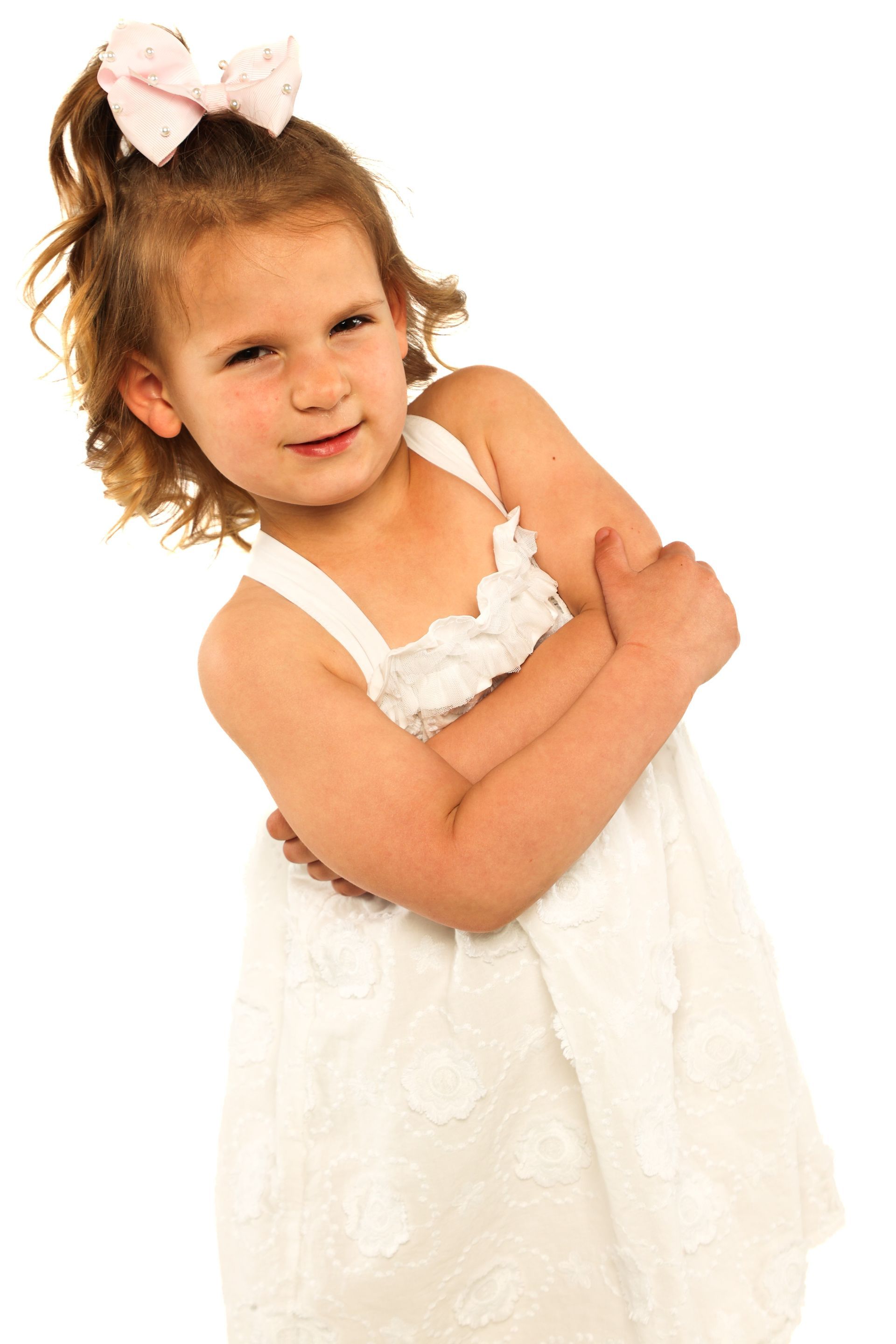 Young child in a white dress with a bow, posing with arms crossed against a white background