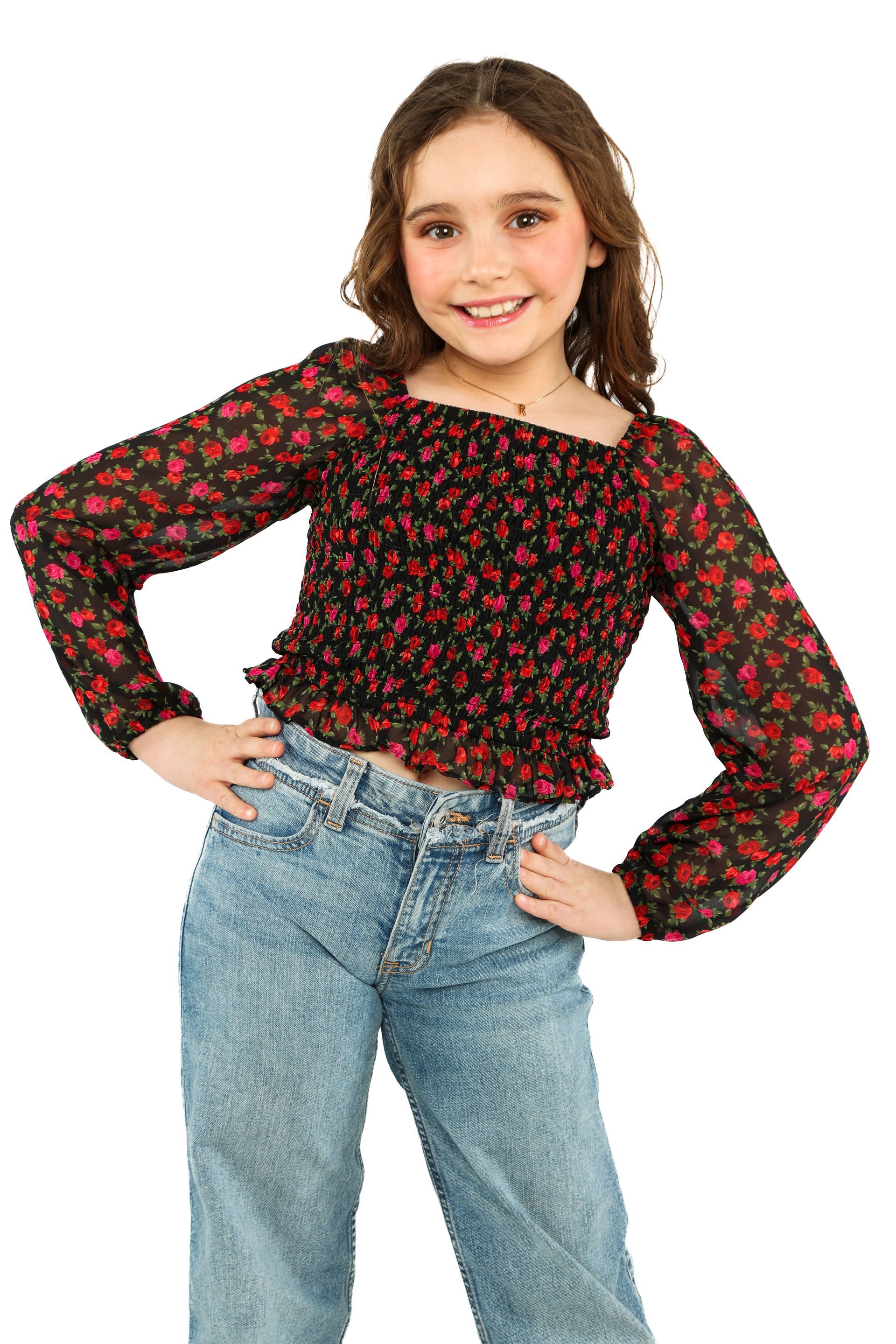 Smiling child posing with hands on hips, wearing a black-and-red floral top and light blue jeans.