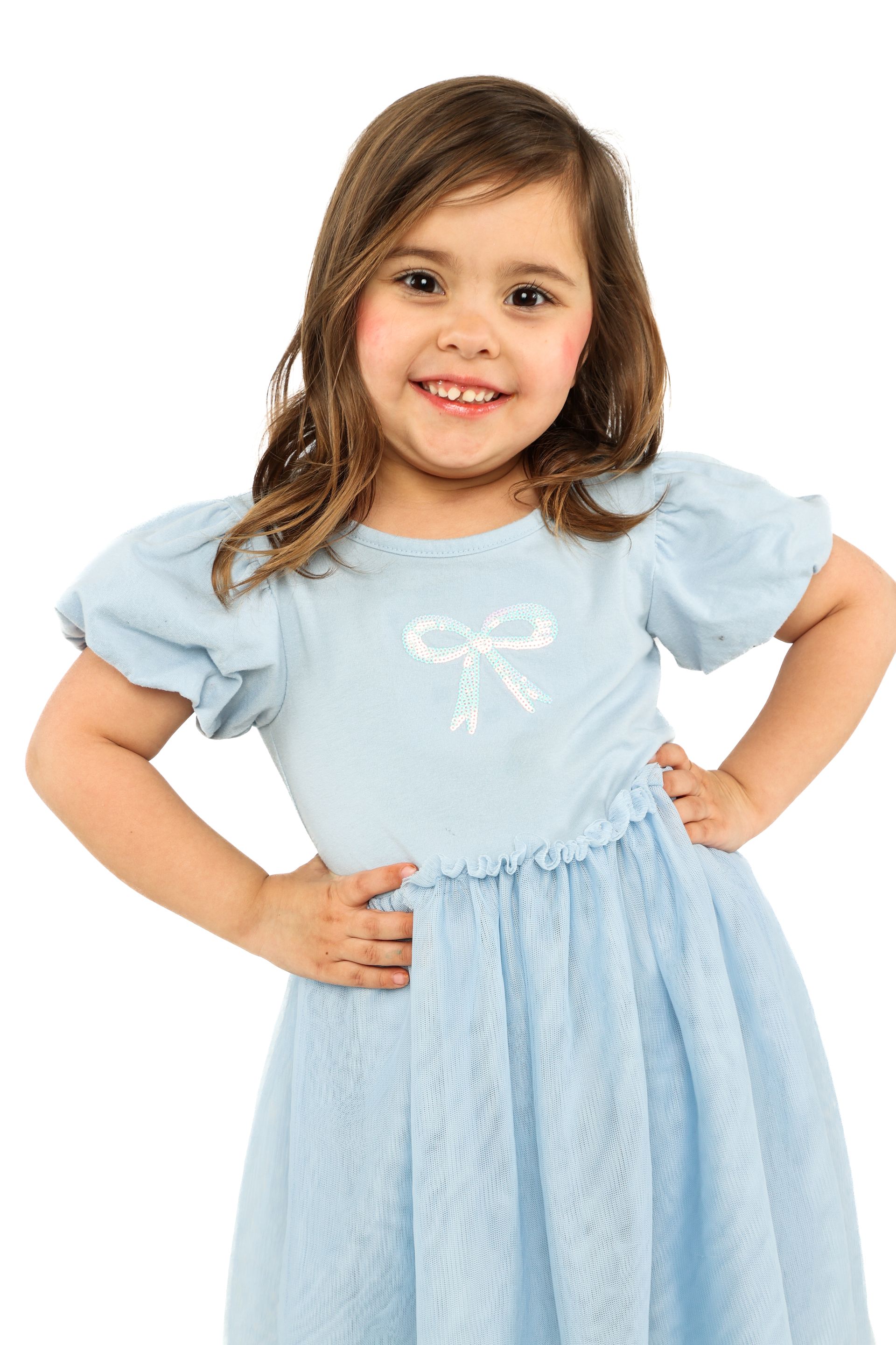 Child in a light blue dress smiling with hands on hips against a white background
