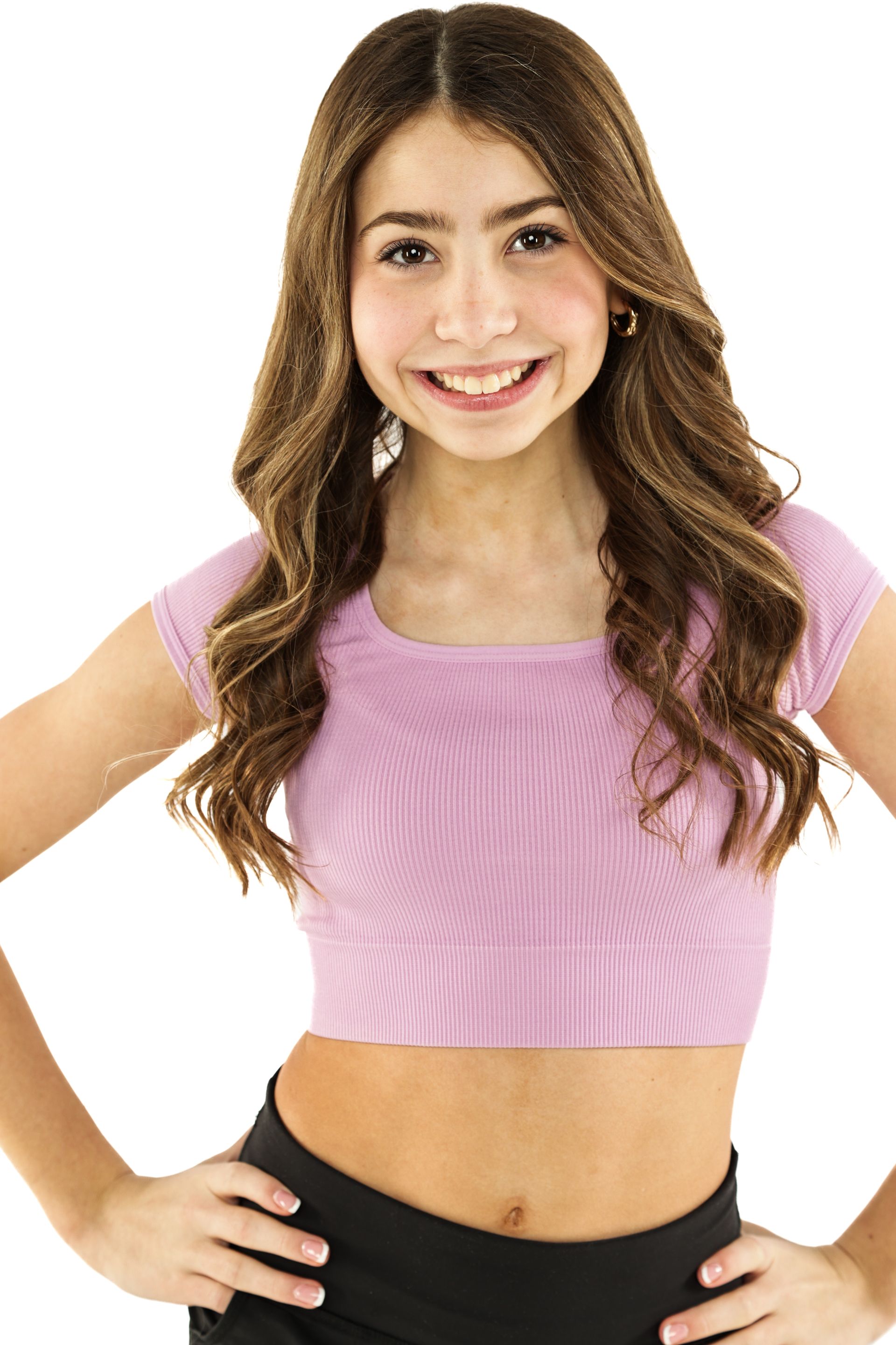 Smiling woman in a pink top and black pants, standing with hands on hips against a white background