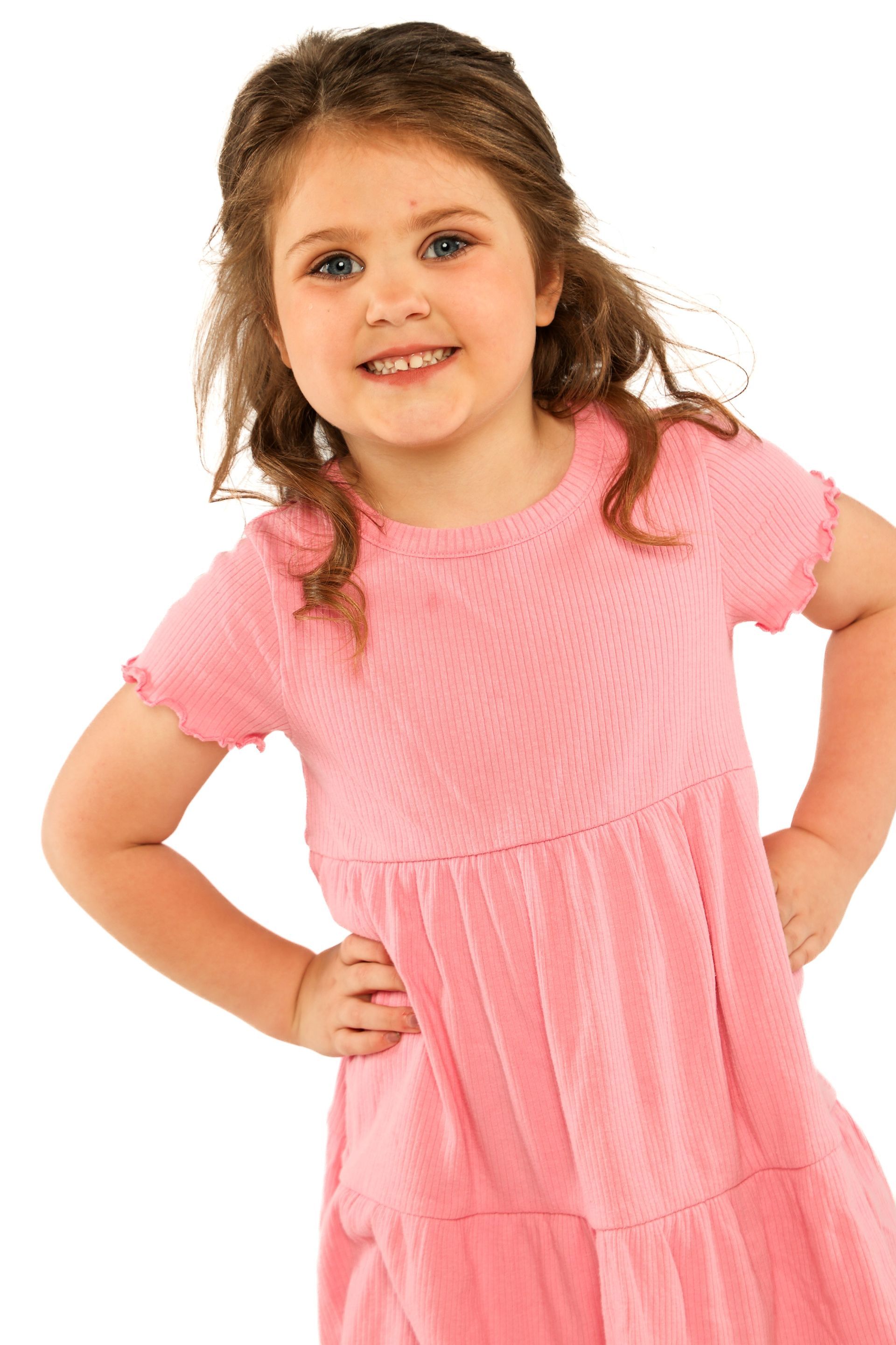Smiling child in a pink dress standing with hands on hips against a white background