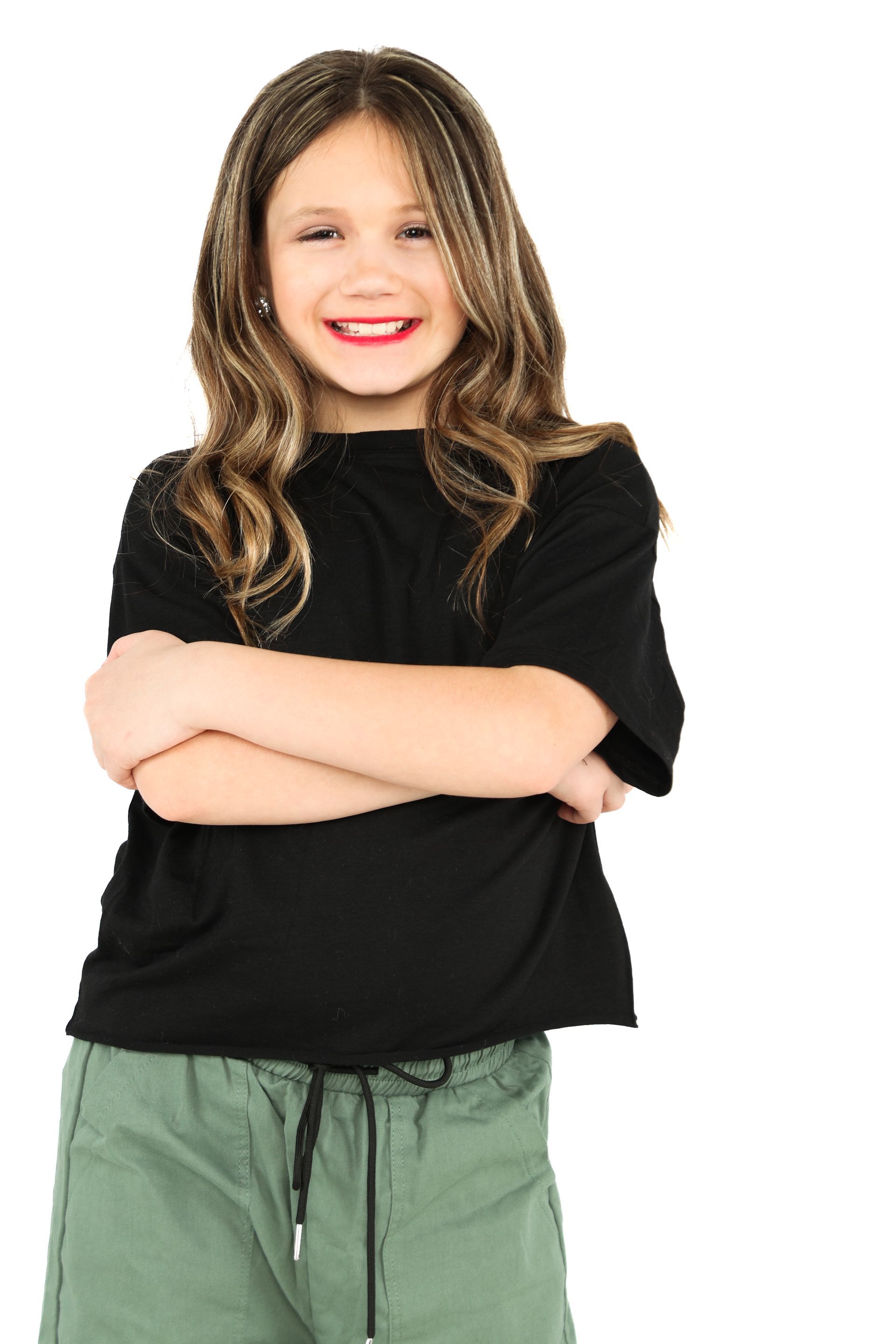 Smiling child with crossed arms, wearing a black shirt and green pants on a white background