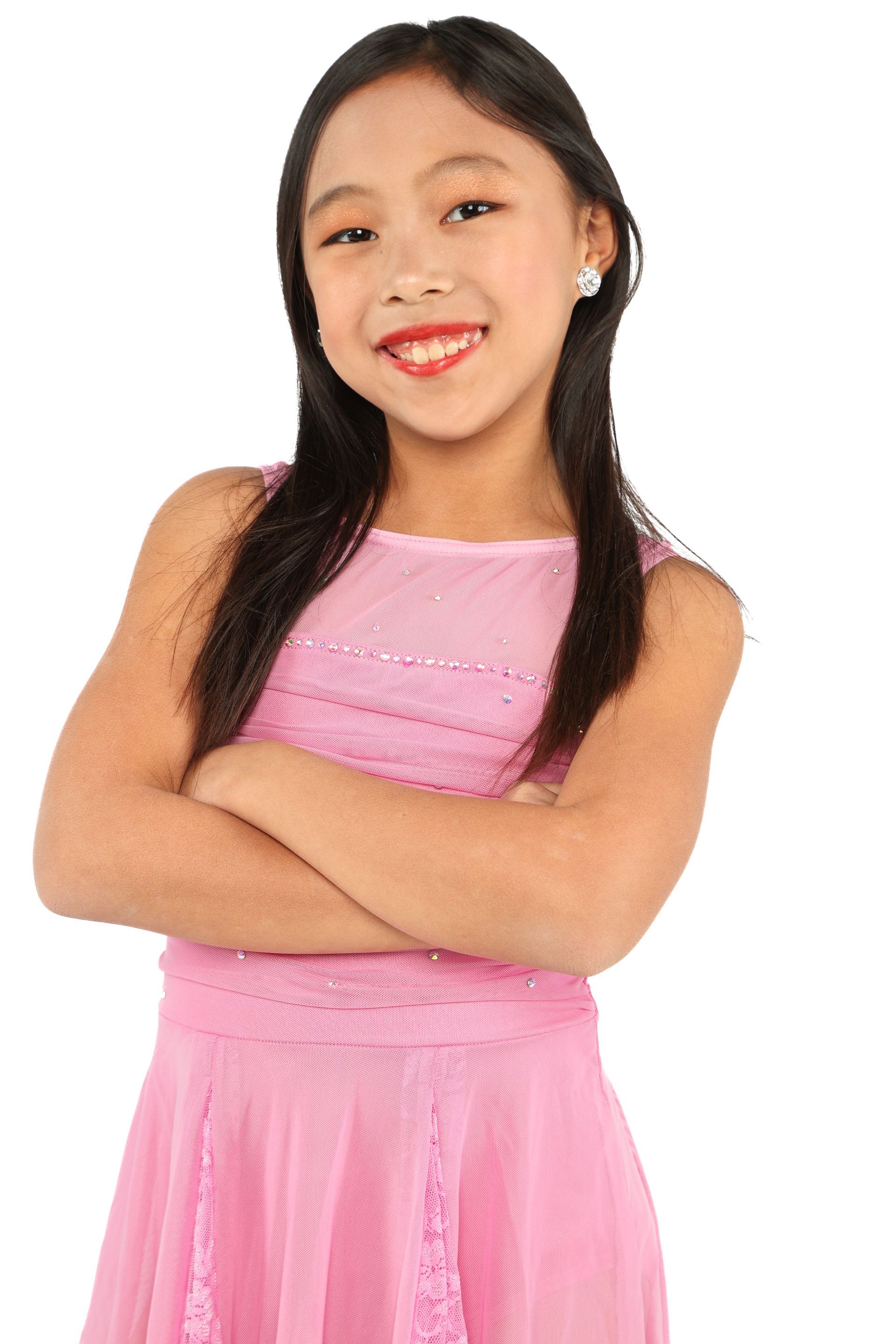 Young girl in a pink dress smiling with arms crossed against a white background