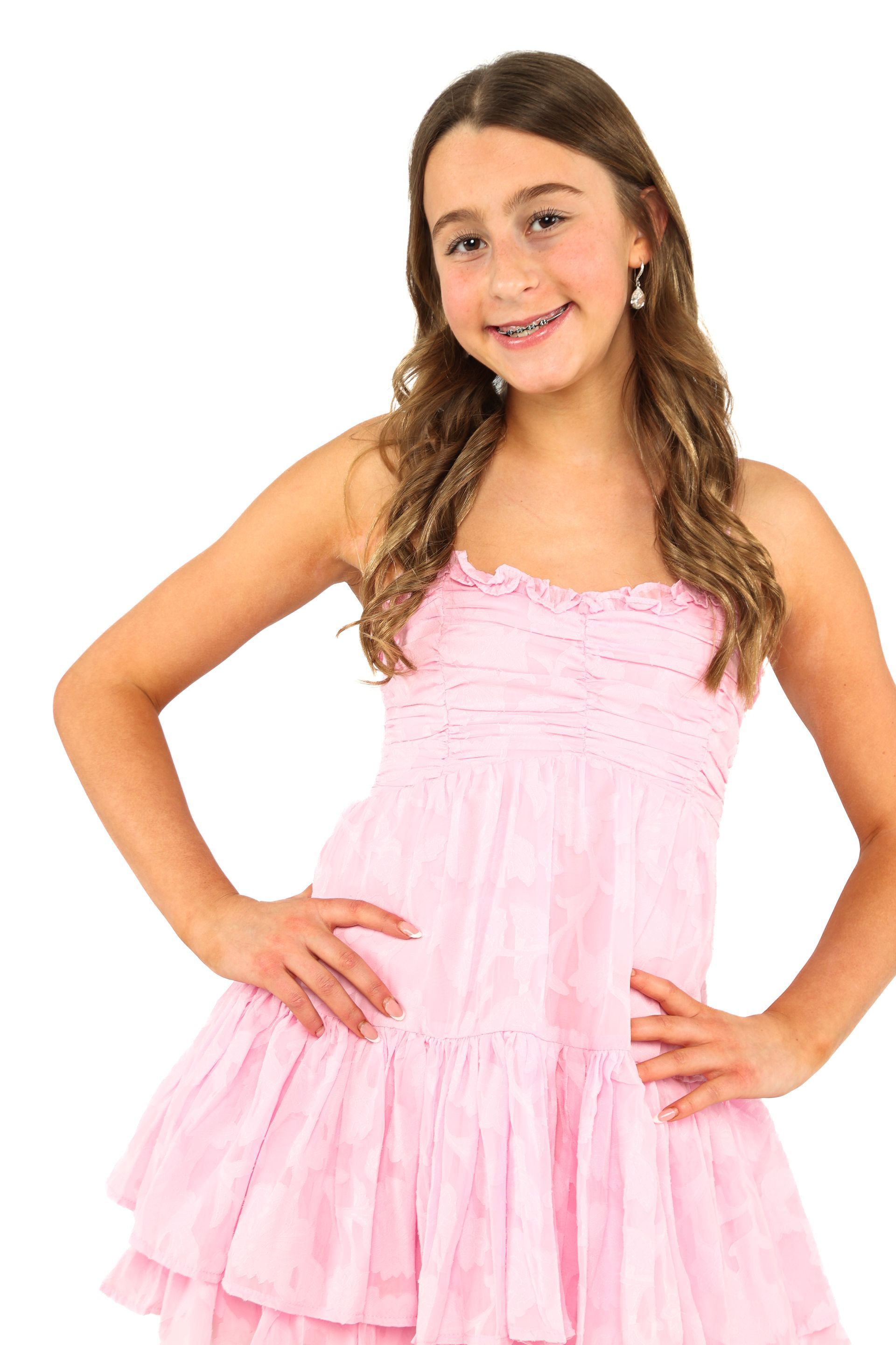 Young girl in a pink dress posing with hands on hips against a white background