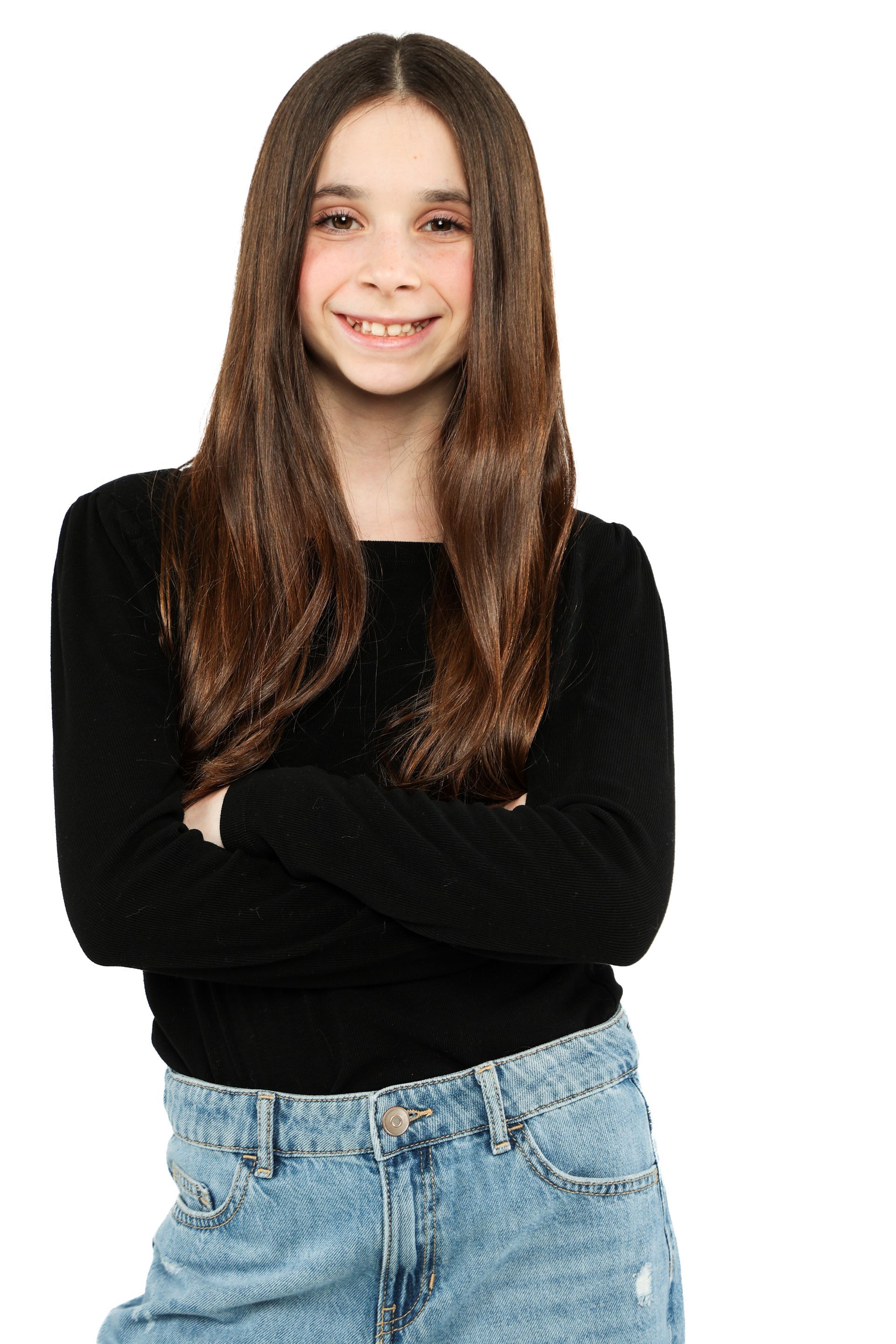 Person with long brown hair in a black top and jeans, standing with arms crossed and smiling on a white background