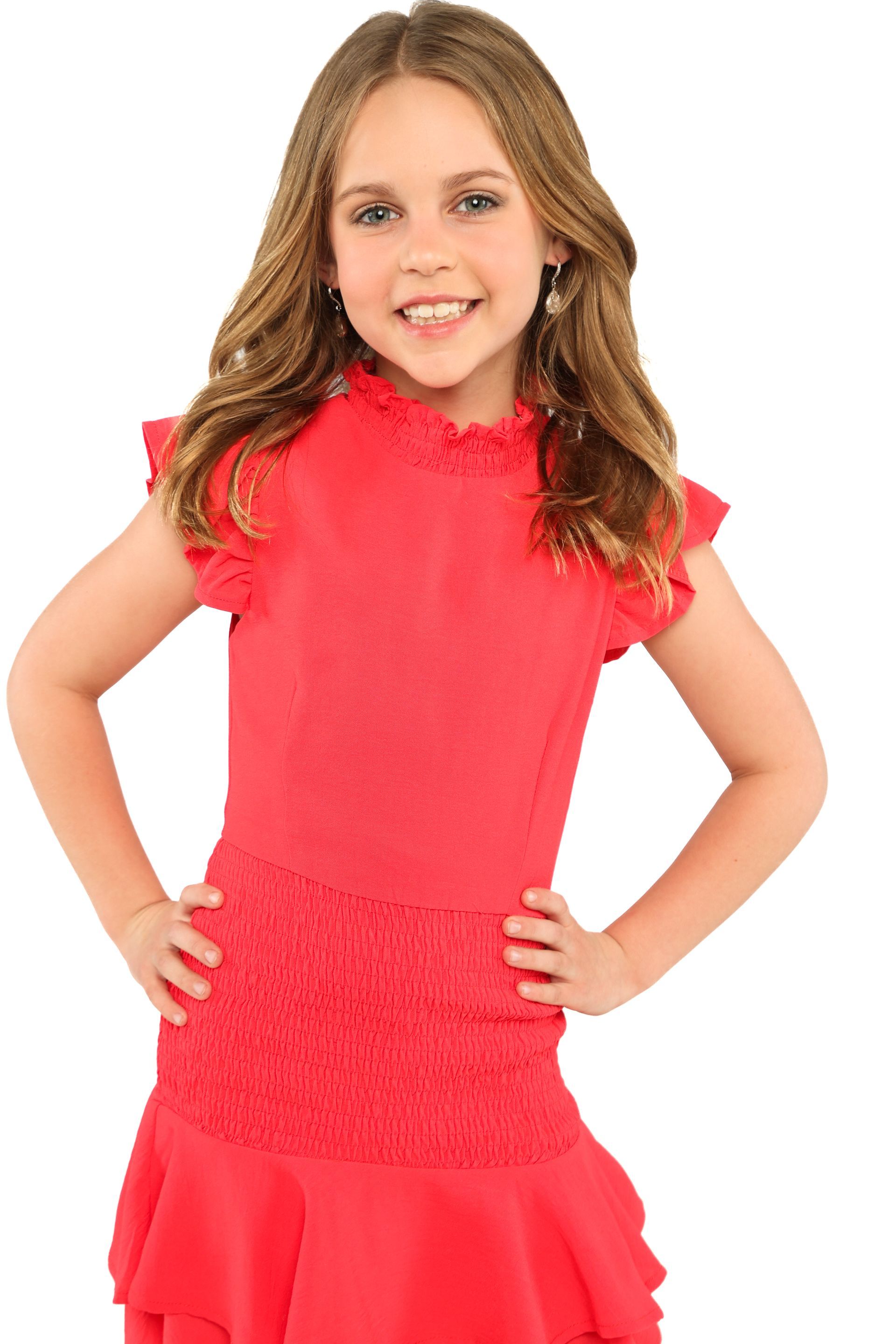 Child wearing a bright pink dress, standing with hands on hips and smiling against a white background