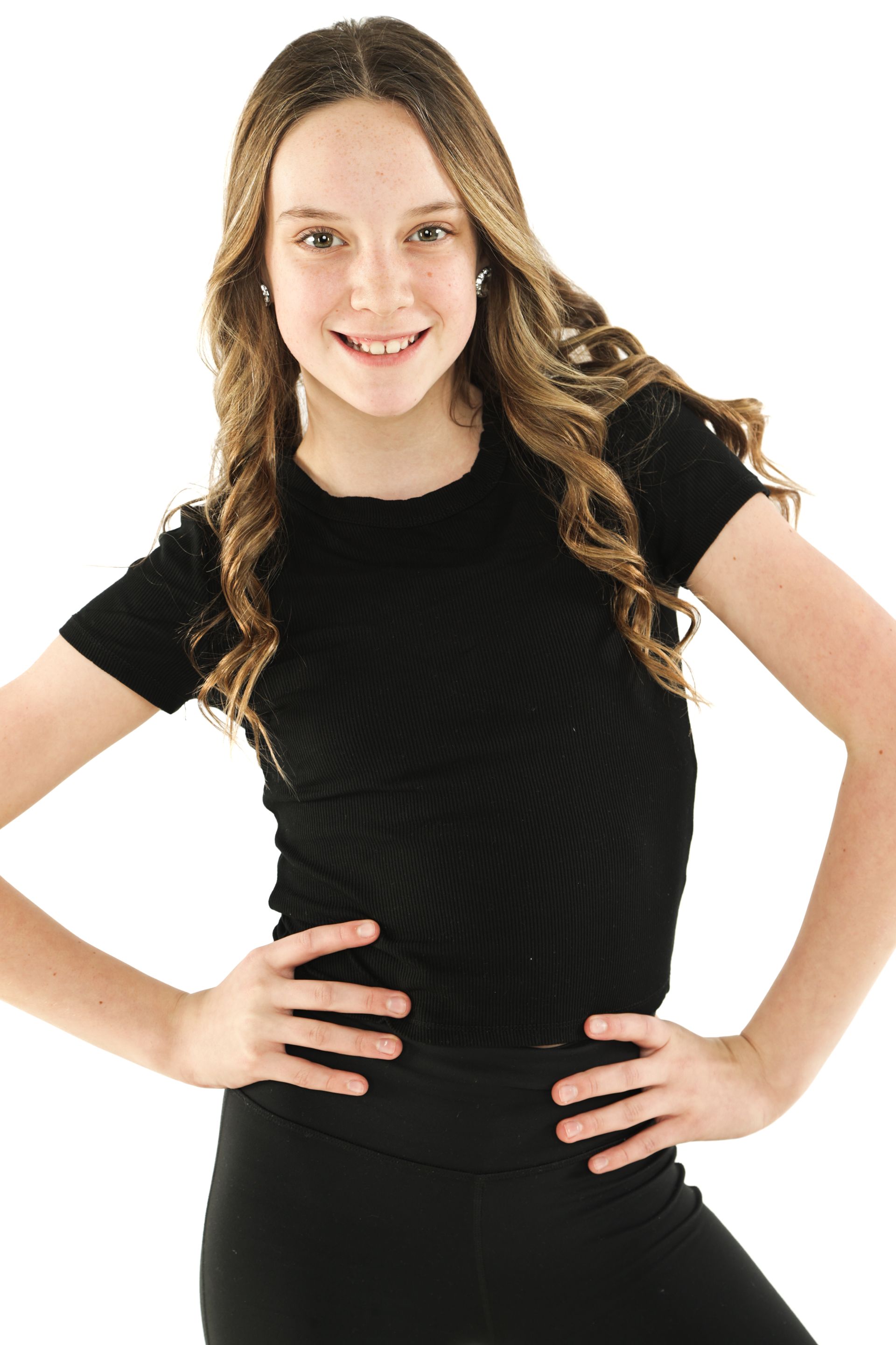Smiling woman in a black shirt and pants, standing with hands on hips against a white background