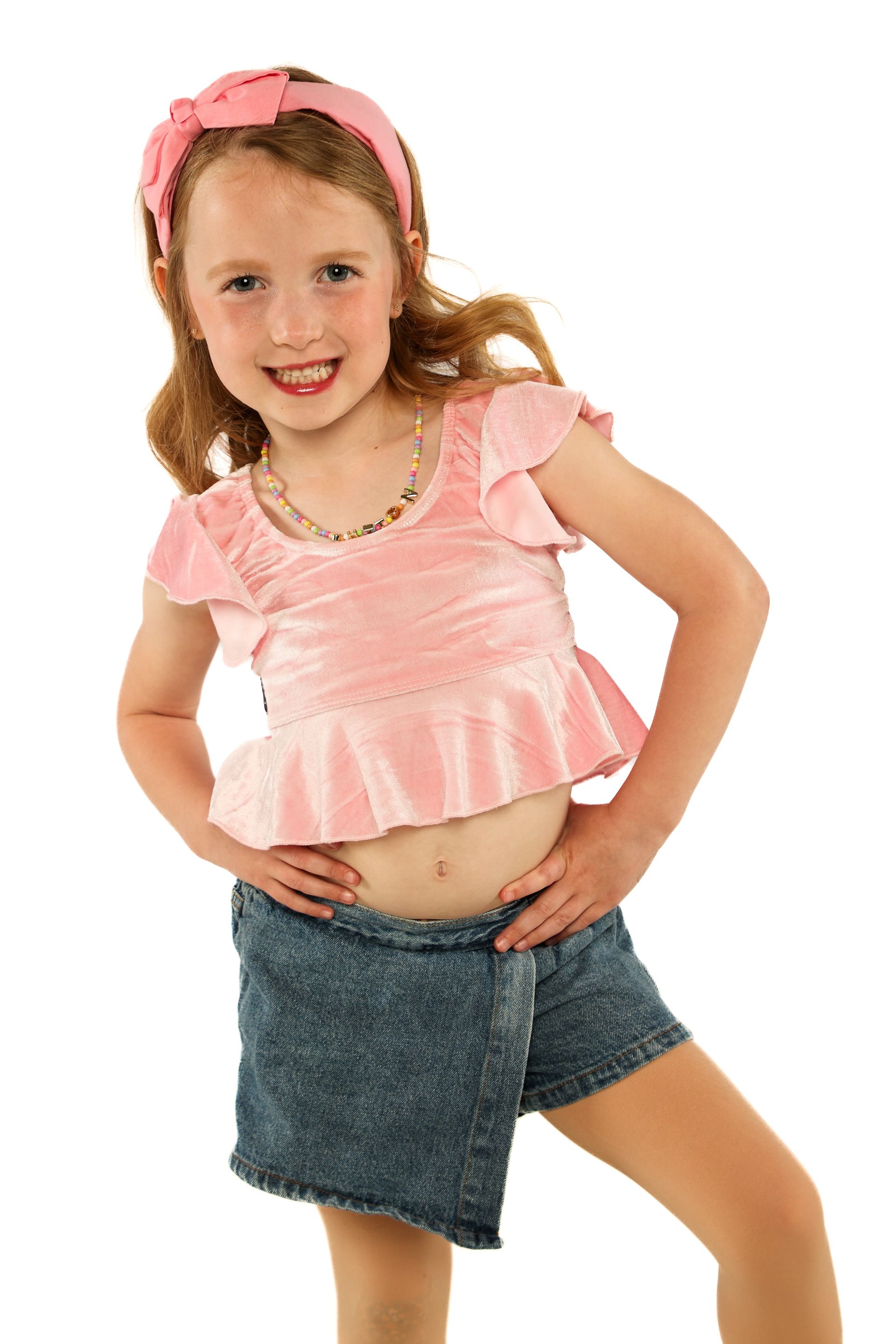 Smiling child in pink shirt and hat, posing with one hand on hip against a white background