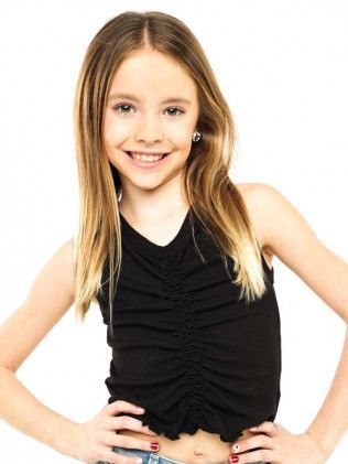 Smiling child in a black sleeveless top, standing with hands on hips against a white background