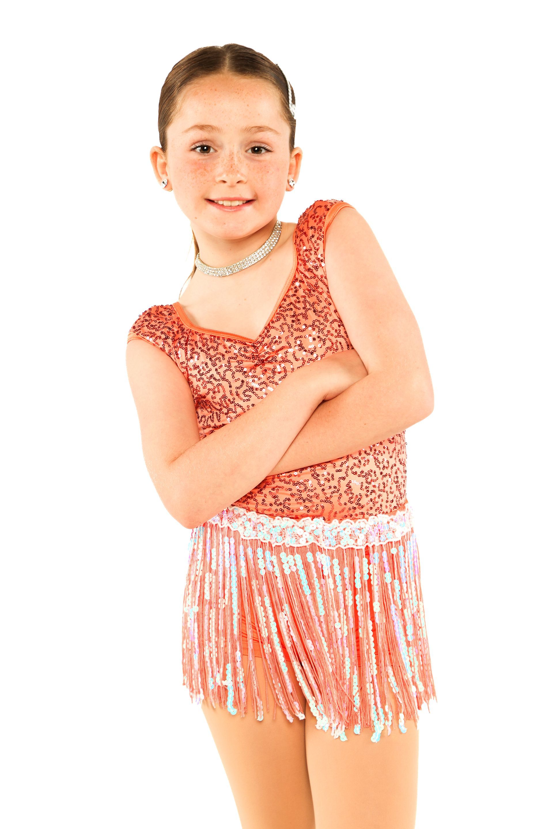 Young dancer in orange sequined costume with fringe, standing against a white background