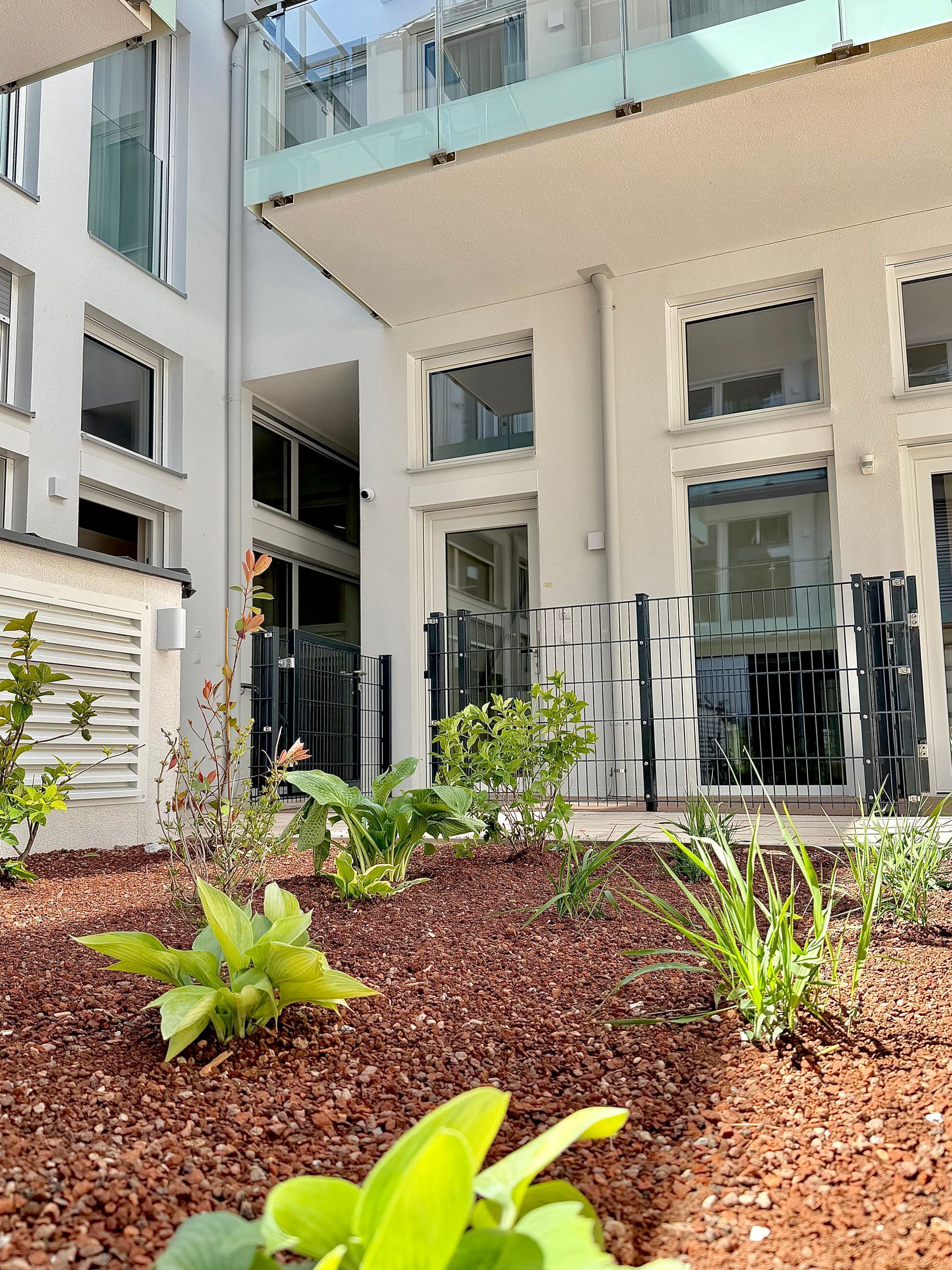 Modern apartment courtyard with landscaped plants, white building facade, and patio seating areas