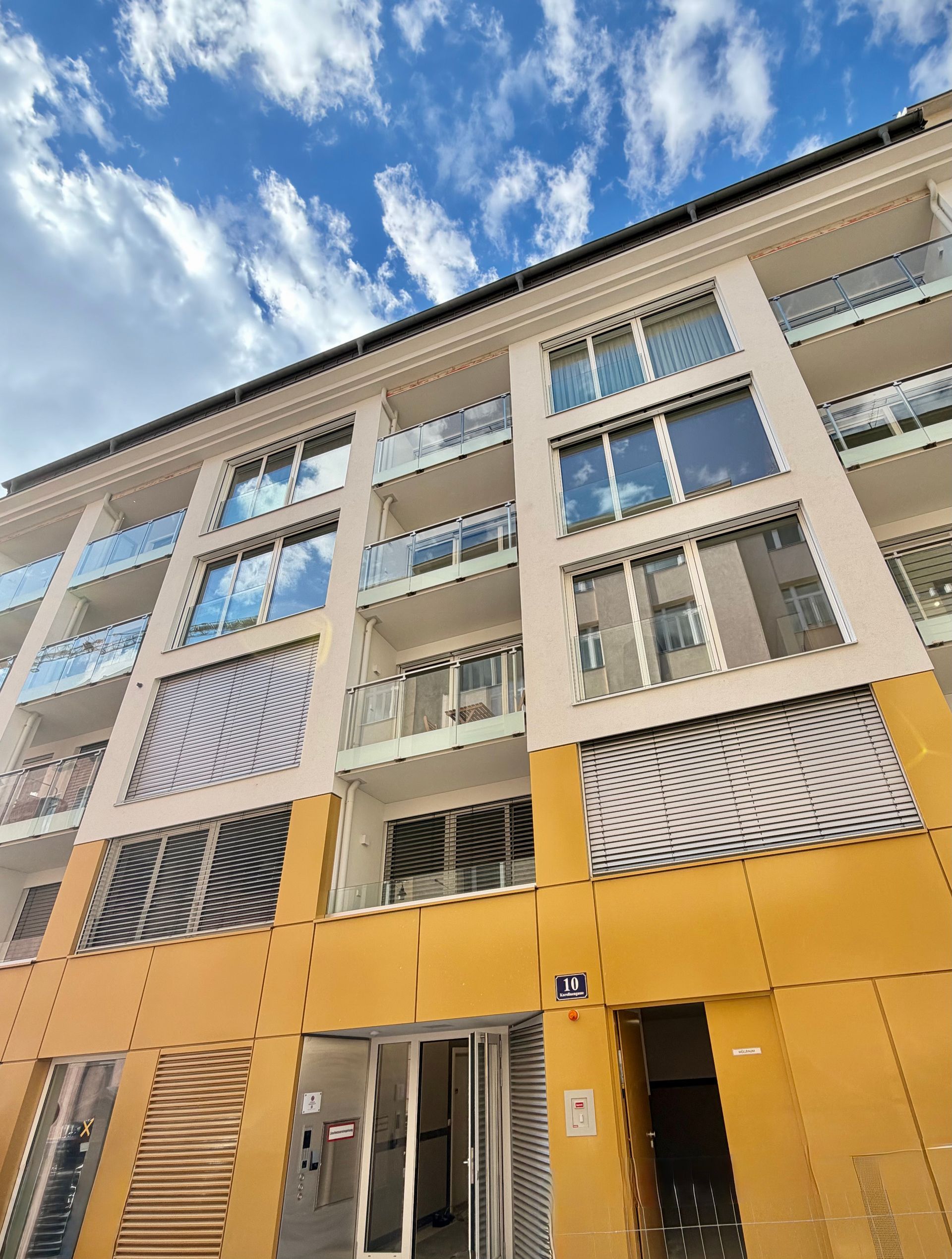 Modern yellow-and-white apartment building viewed from below against a blue sky with clouds
