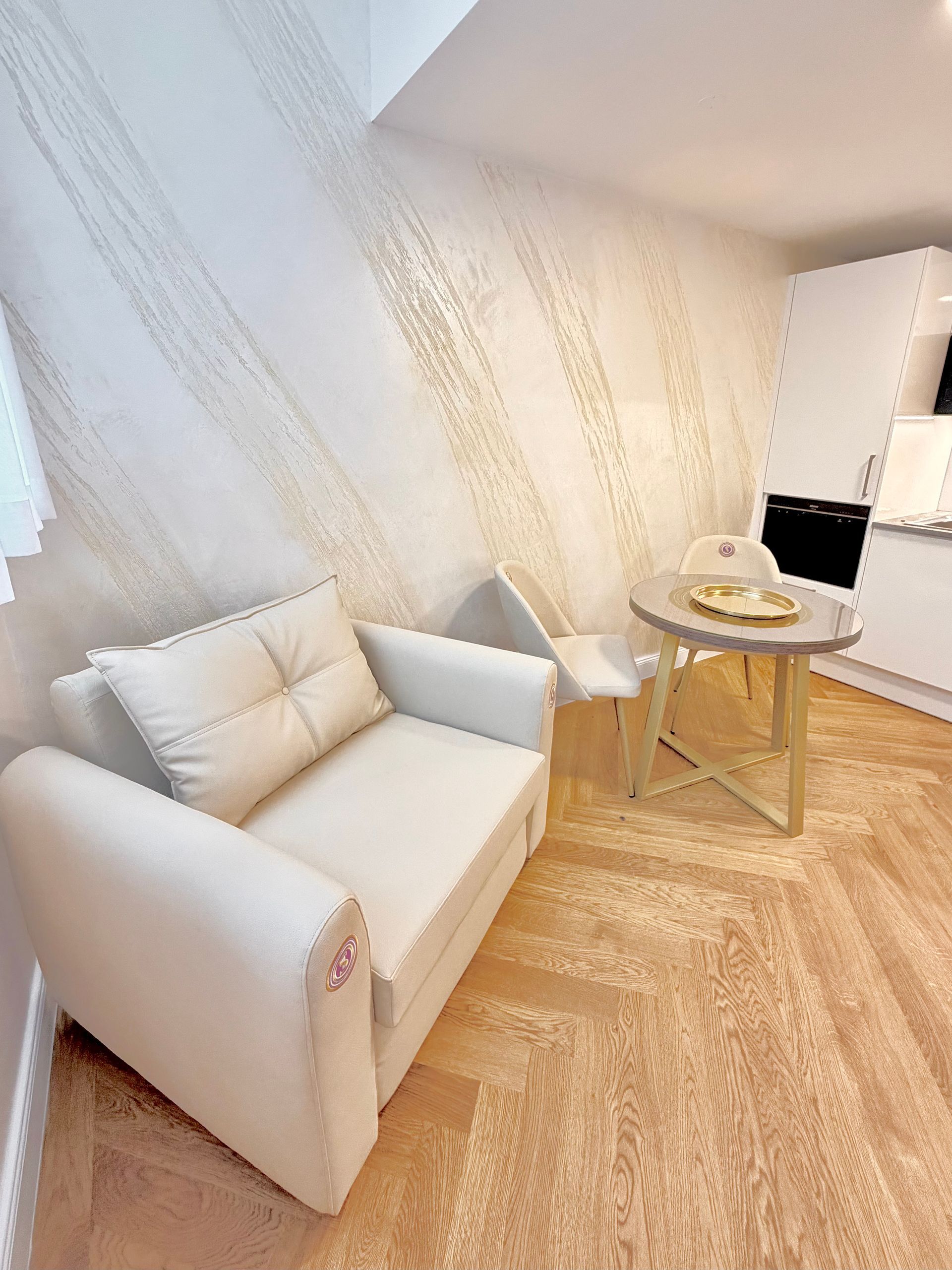 Minimalist white lounge chair and round side table in a bright room with sheer curtains and herringbone wood floor