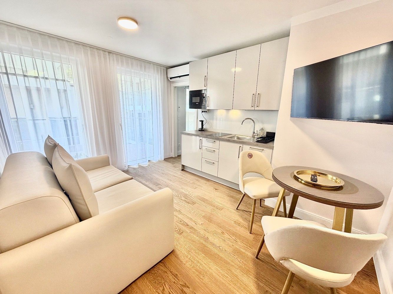 Bright modern studio apartment with sofa, kitchenette, dining nook, and wall-mounted TV