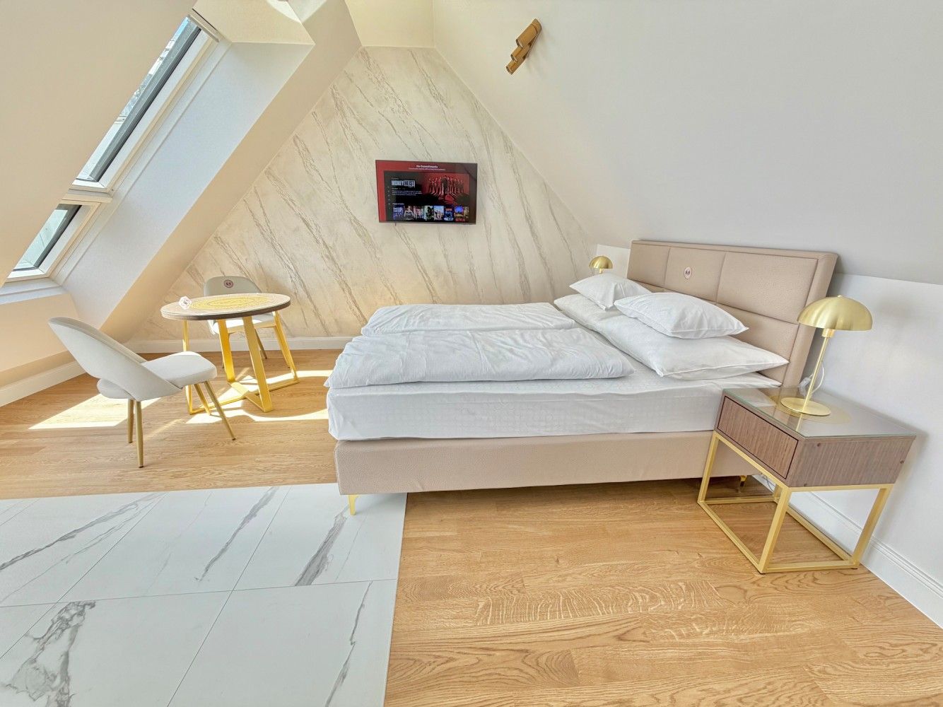 Bright attic bedroom with a made bed, skylight, small table, and light wood floors