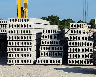 Stacks of white concrete slabs with oval holes in a gravel yard under a blue sky.