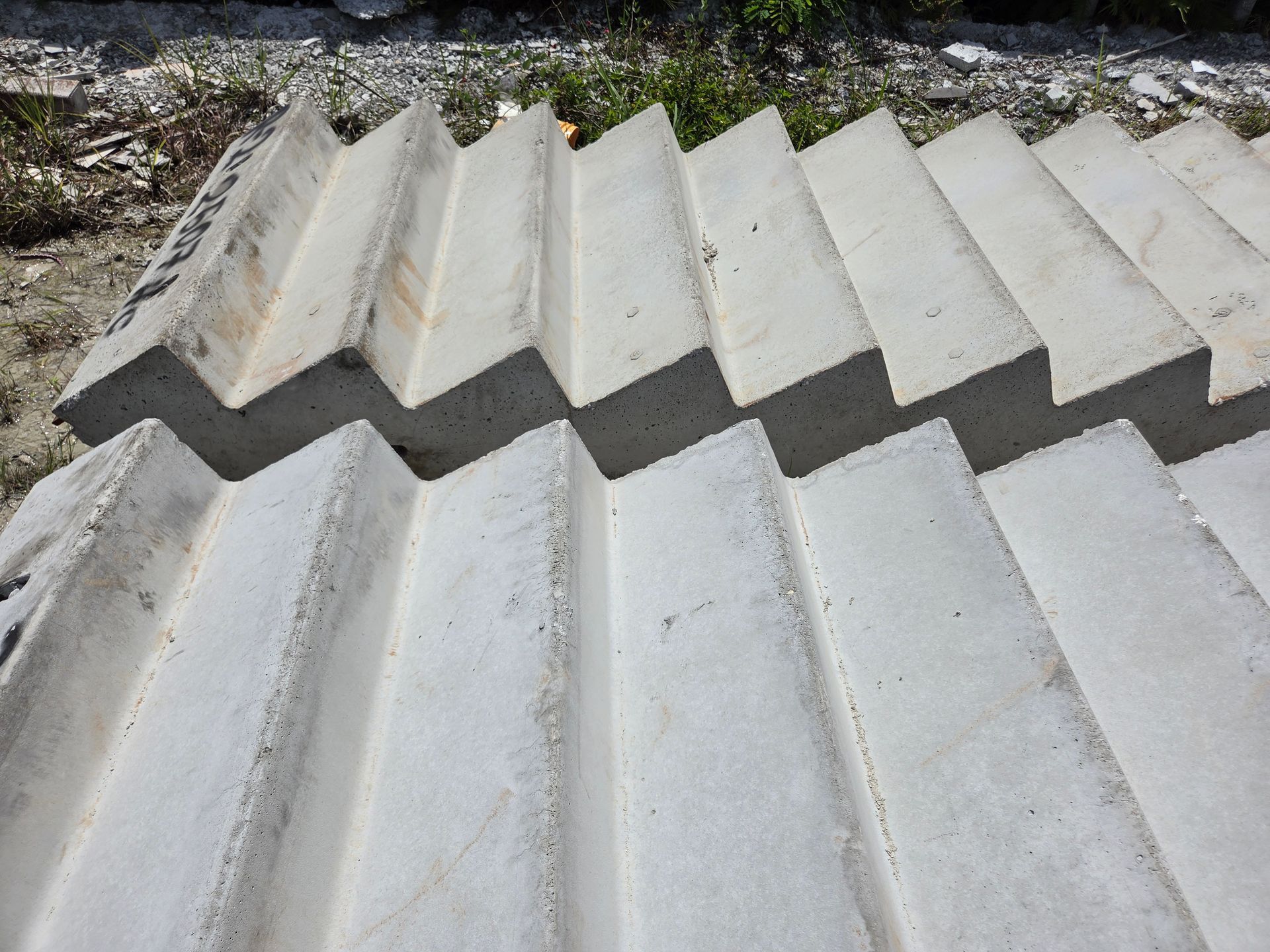 White corrugated roofing panels stacked outdoors on rocky ground