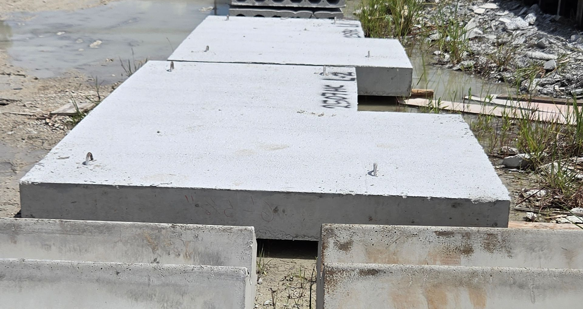Stacked gray concrete slabs on a sidewalk beside water and weeds