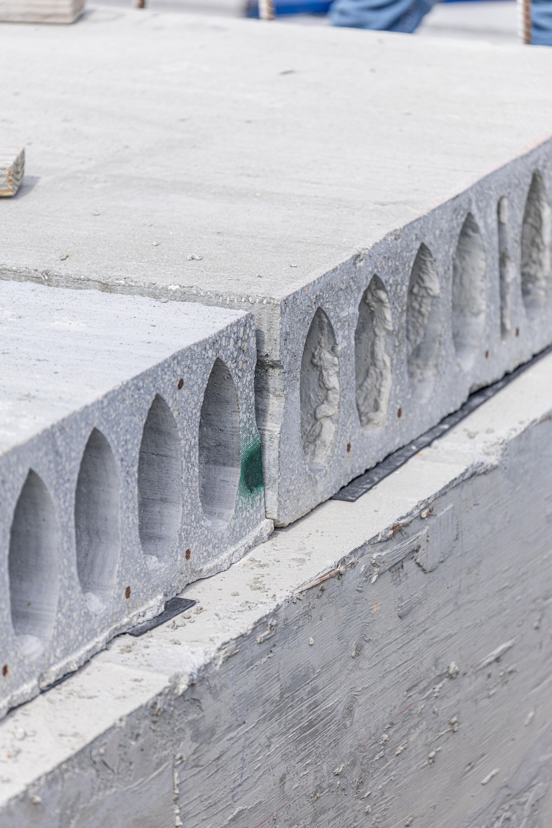Gray concrete hollow-core slab with visible voids, stacked on a construction site.