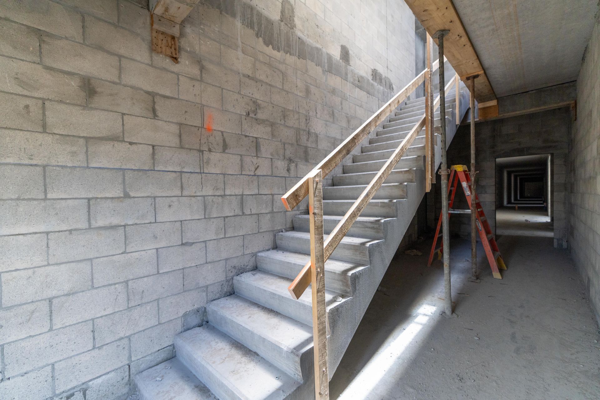Unfinished stairway with wooden railing in a cinder block building interior