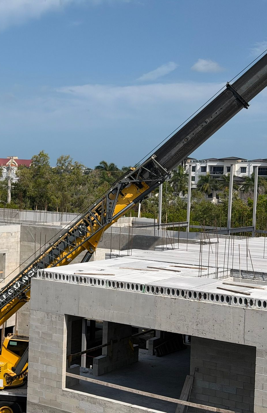 Construction site with a yellow crane boom lifting a concrete slab over a partially built structure.