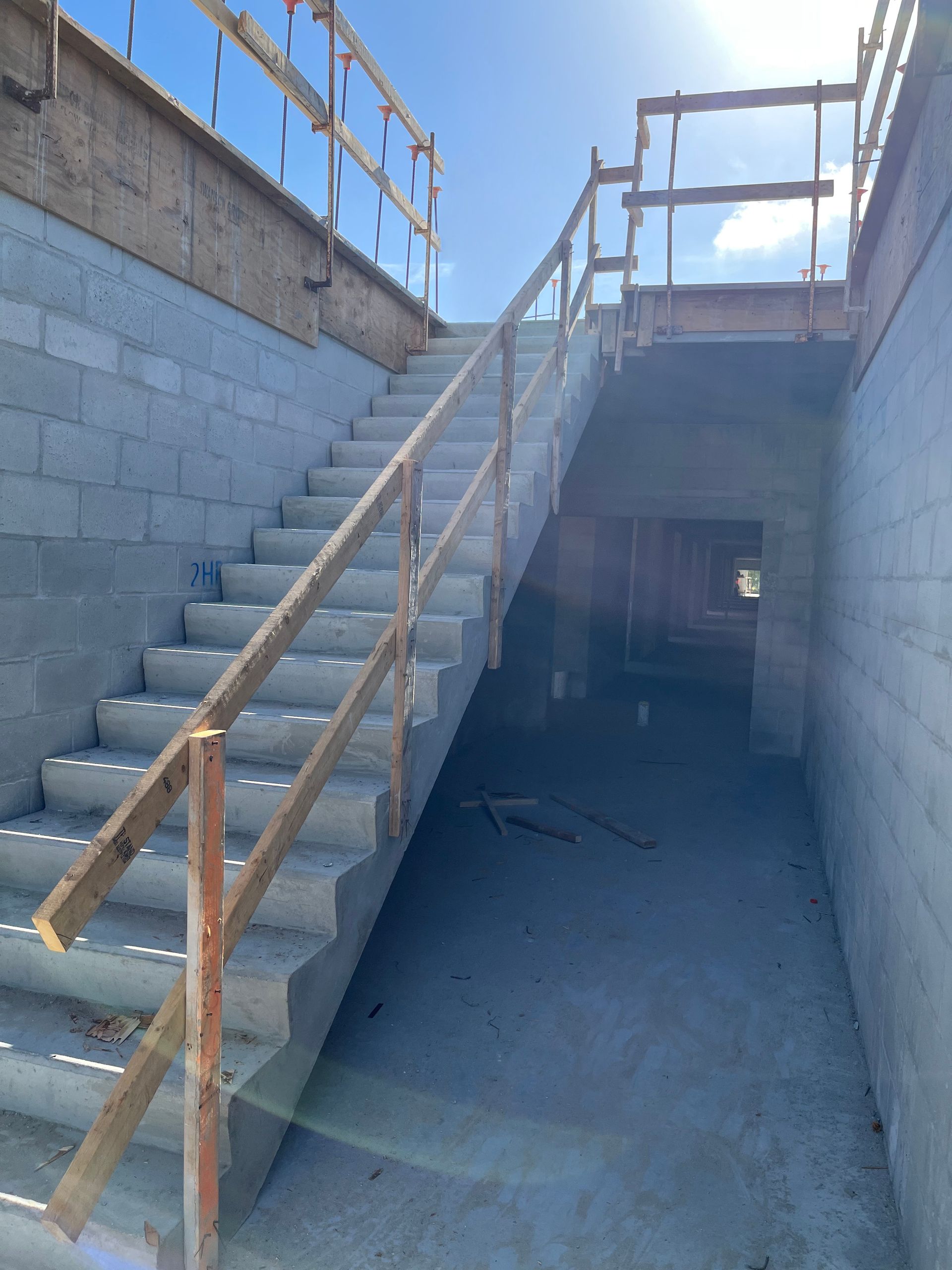 Concrete stairway descending into an unfinished basement with cinder block walls and a wooden handrail.