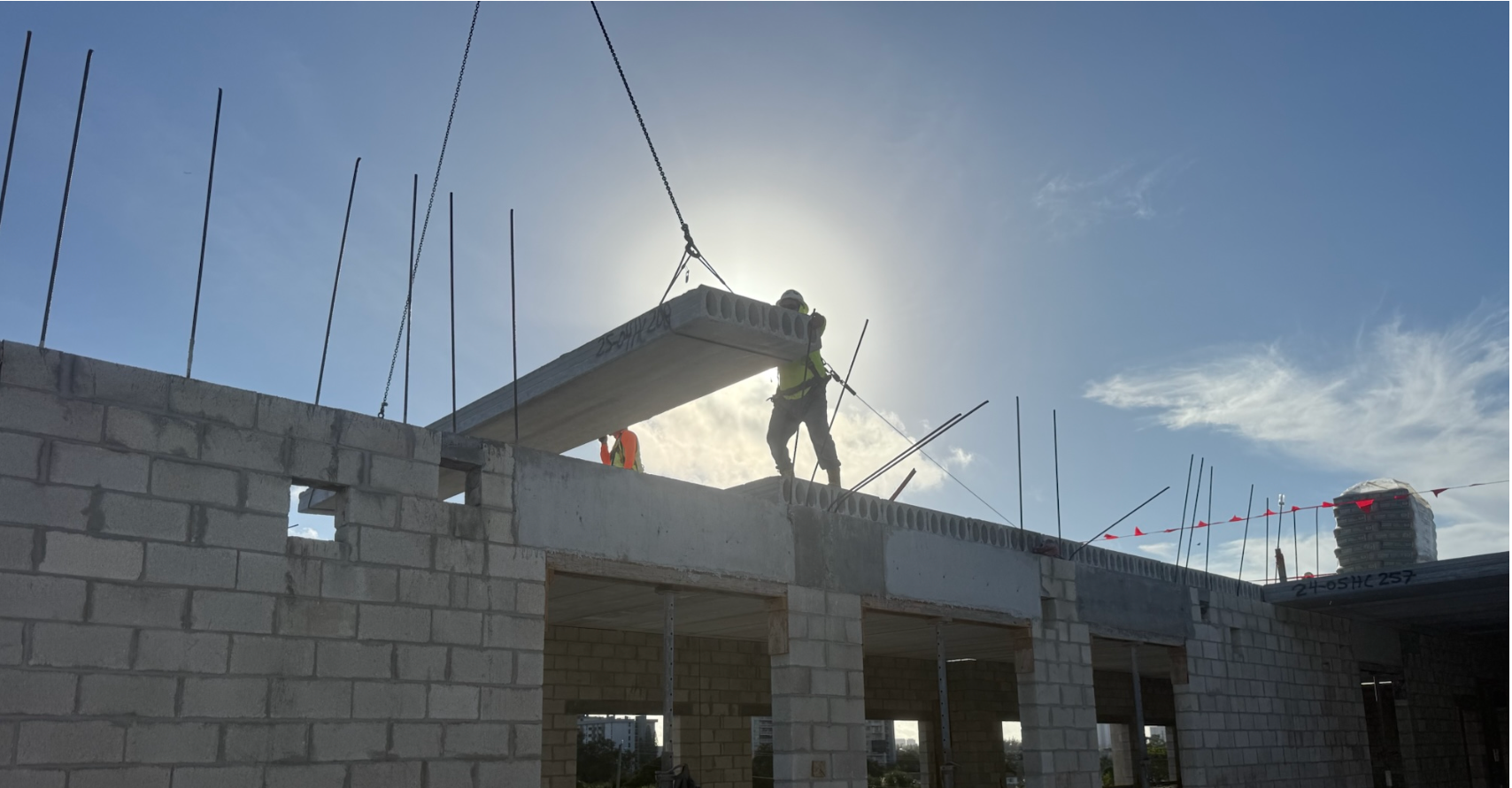 Worker on a rooftop construction site, silhouetted against the sun, with a partially built brick wall below.