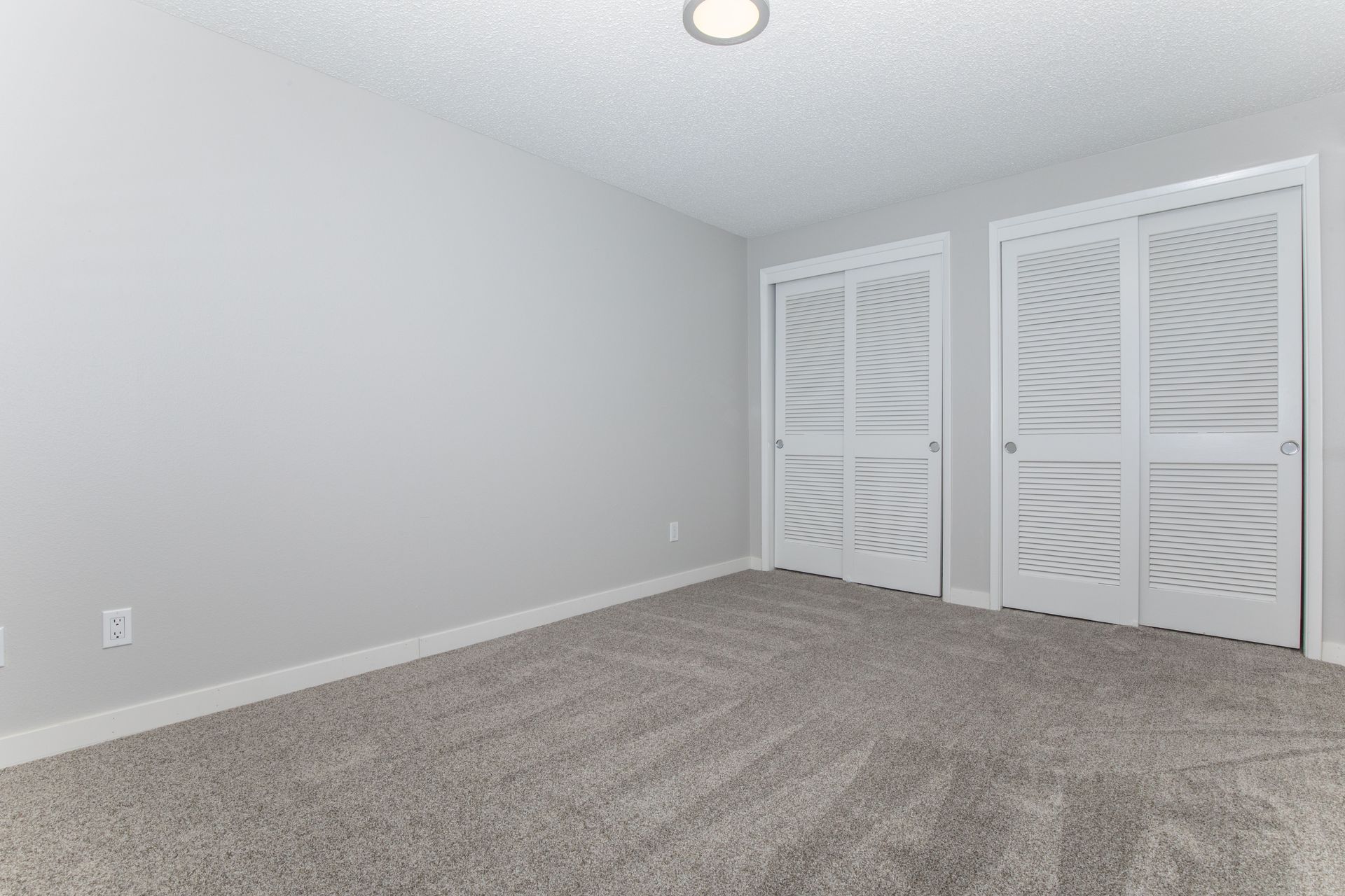 An empty bedroom with a carpeted floor and sliding glass doors.