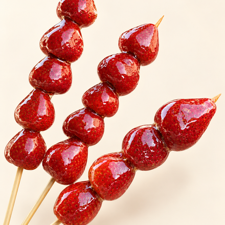 Red candied fruit skewers on wooden sticks against a light background