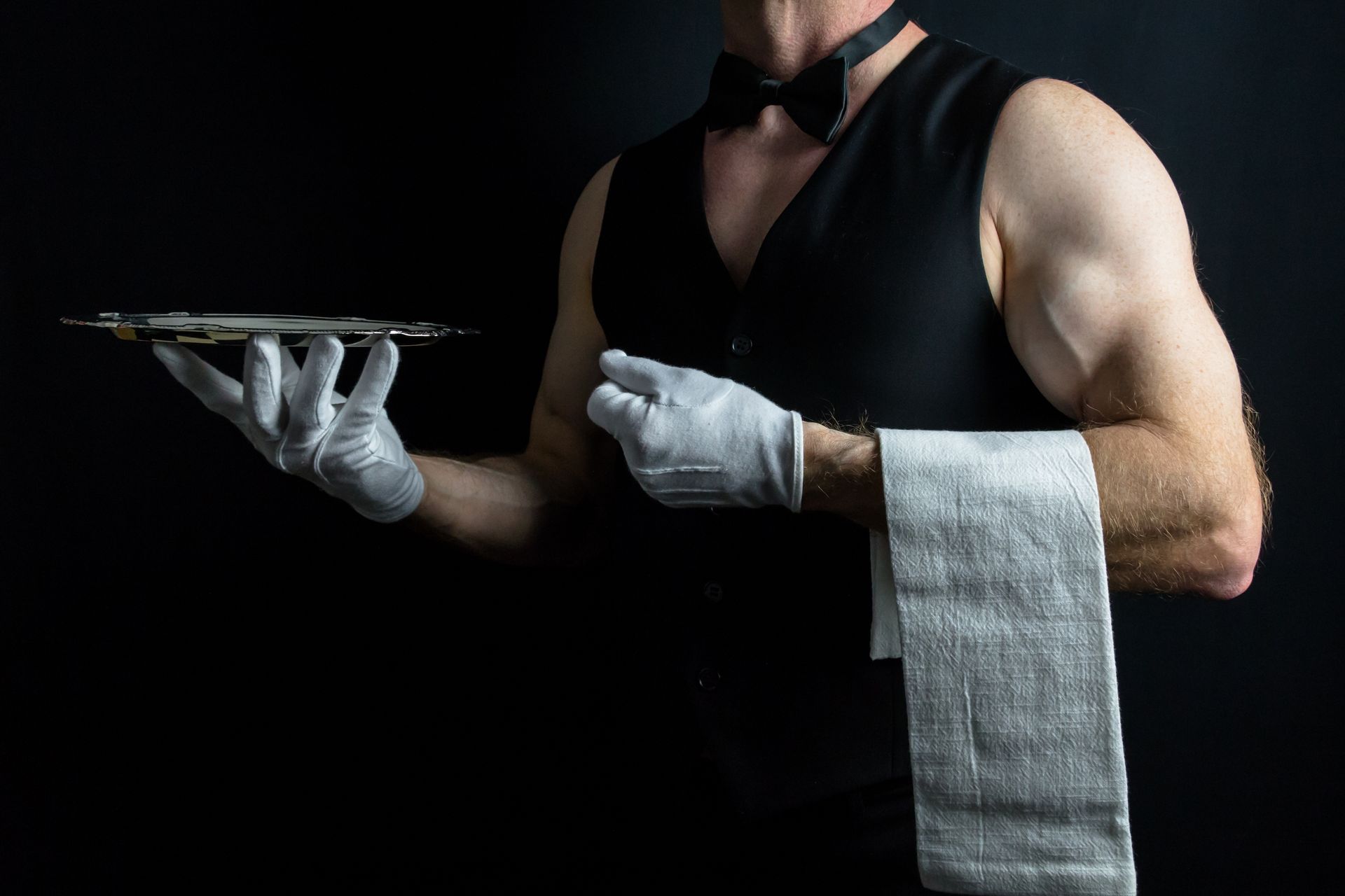 Buff butler wearing a bow tie and gloves holding a serving tray