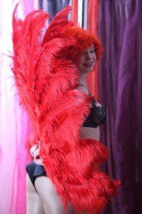 A burlesque performer hidden behind oversized ostrich feather fans, preparing for a dramatic reveal, showcasing classic vintage burlesque tease and stage presence