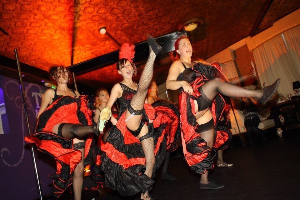 Women performing a Can Can dance routine at a hen party, wearing red and black skirts and kicking in sync on a stage