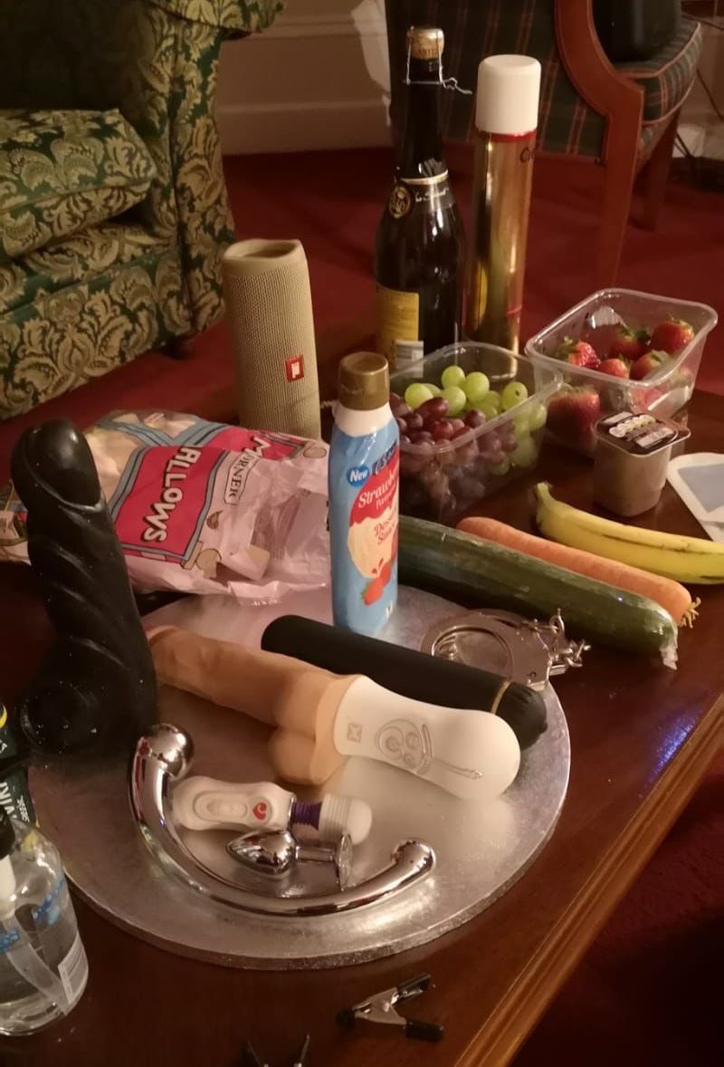 Sex toy party display with vibrators, dildos, whipped cream, fruit, handcuffs and playful props laid out on a table for a lesbian party show by Epic Moments UK.