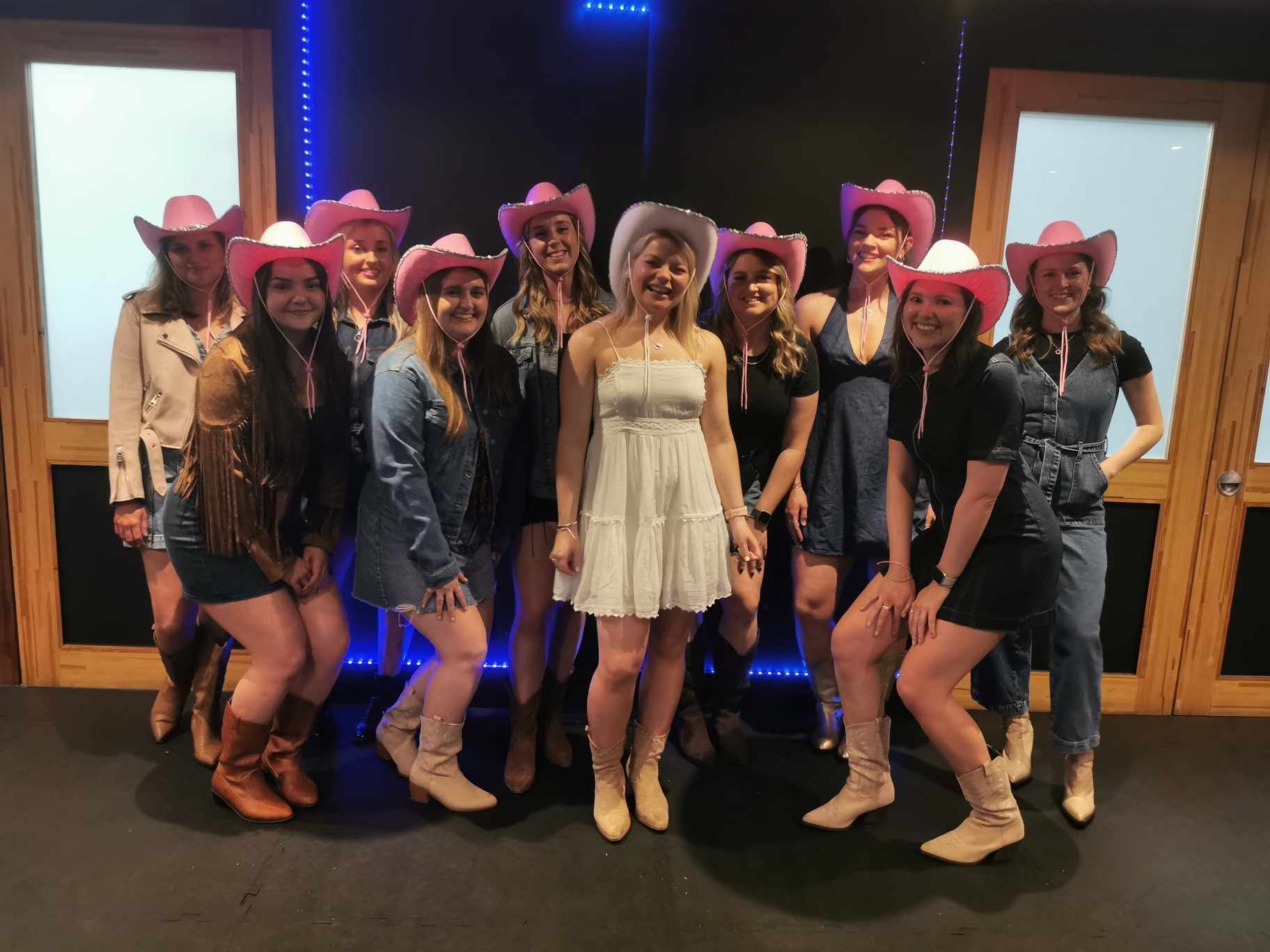 Group of women wearing pink cowboy hats and boots at a Beyoncé Texas Hold ’Em themed hen party dance class, posing together in a studio with country line dancing vibes