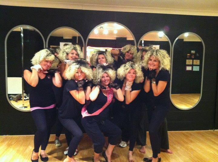 Group of women dressed in Madonna inspired outfits at a hen party dance class, posing together in a studio with retro pop style