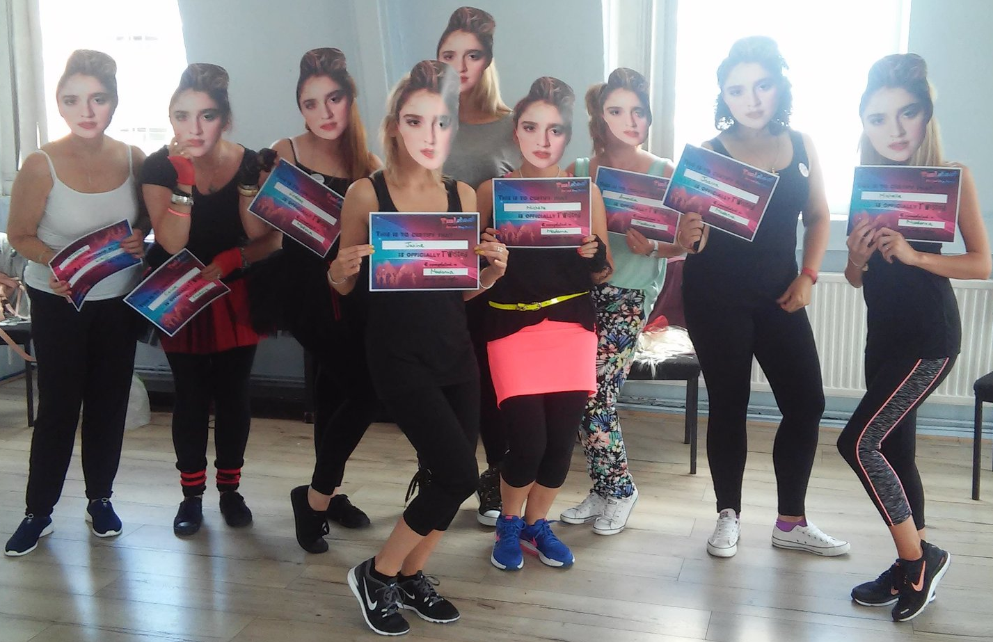Group of women at a hen party dance class in a studio, wearing black outfits and holding certificates, posing together after completing a fun Madonna themed dance routine.