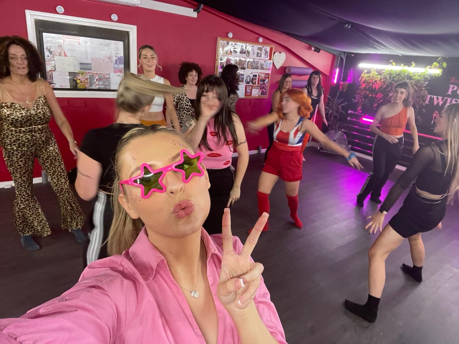 Group of women dancing at a Spice Girls themed hen party dance class, wearing fun outfits and enjoying a lively pop routine in a studio