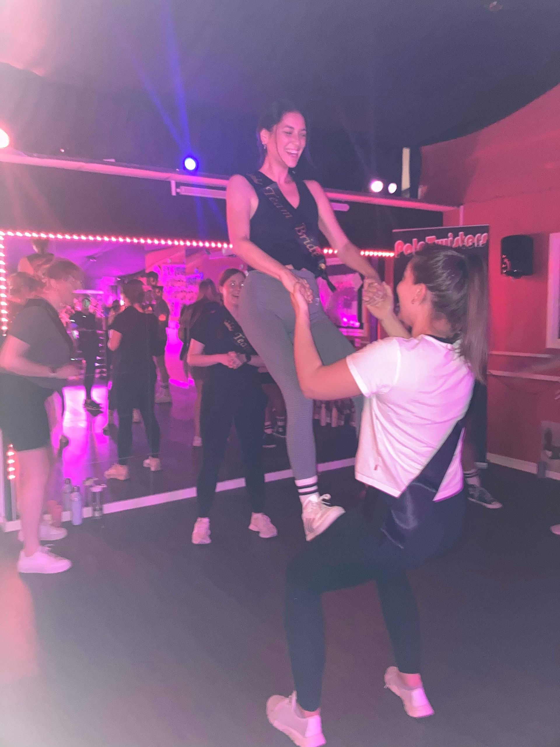 Women performing a lift during a Greatest Showman themed hen party dance class, enjoying a fun group routine in a studio with colourful lighting