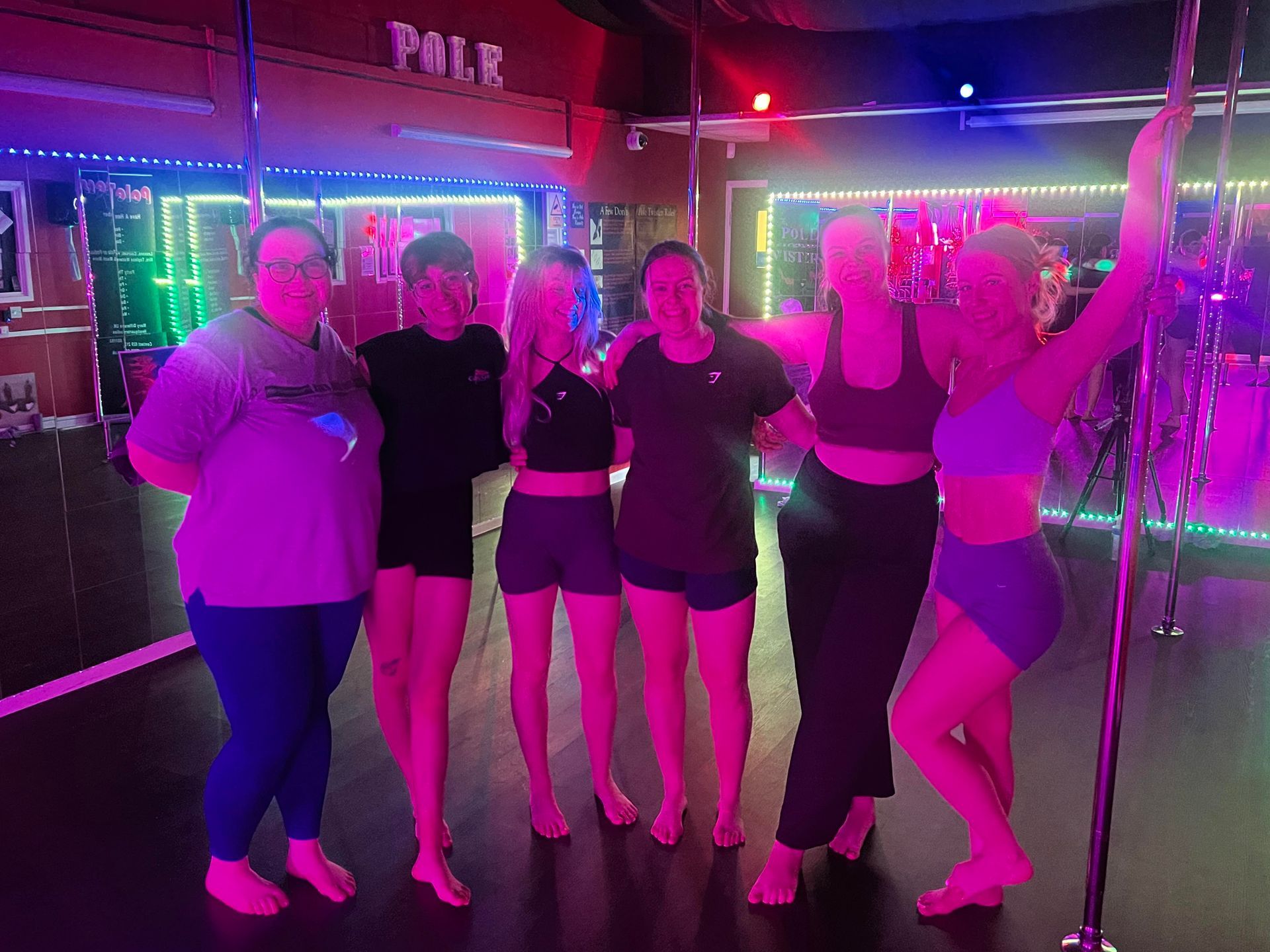 Group of friends standing together at a pole dancing party in a Cardiff studio, smiling under colourful studio lighting