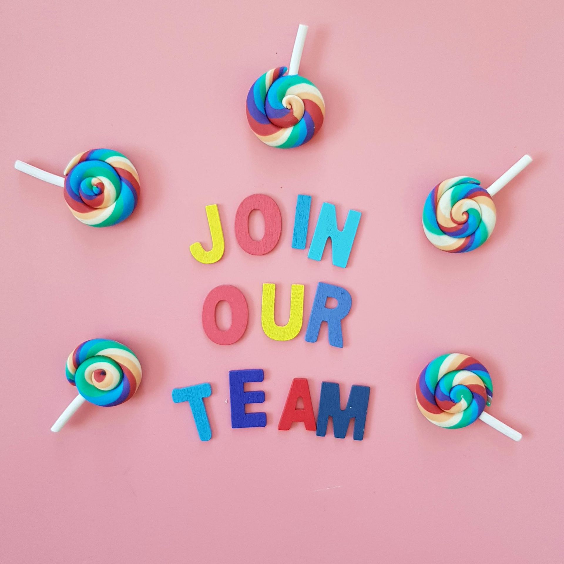 Join our team message displayed with colourful letters on a pink background surrounded by rainbow lollipops