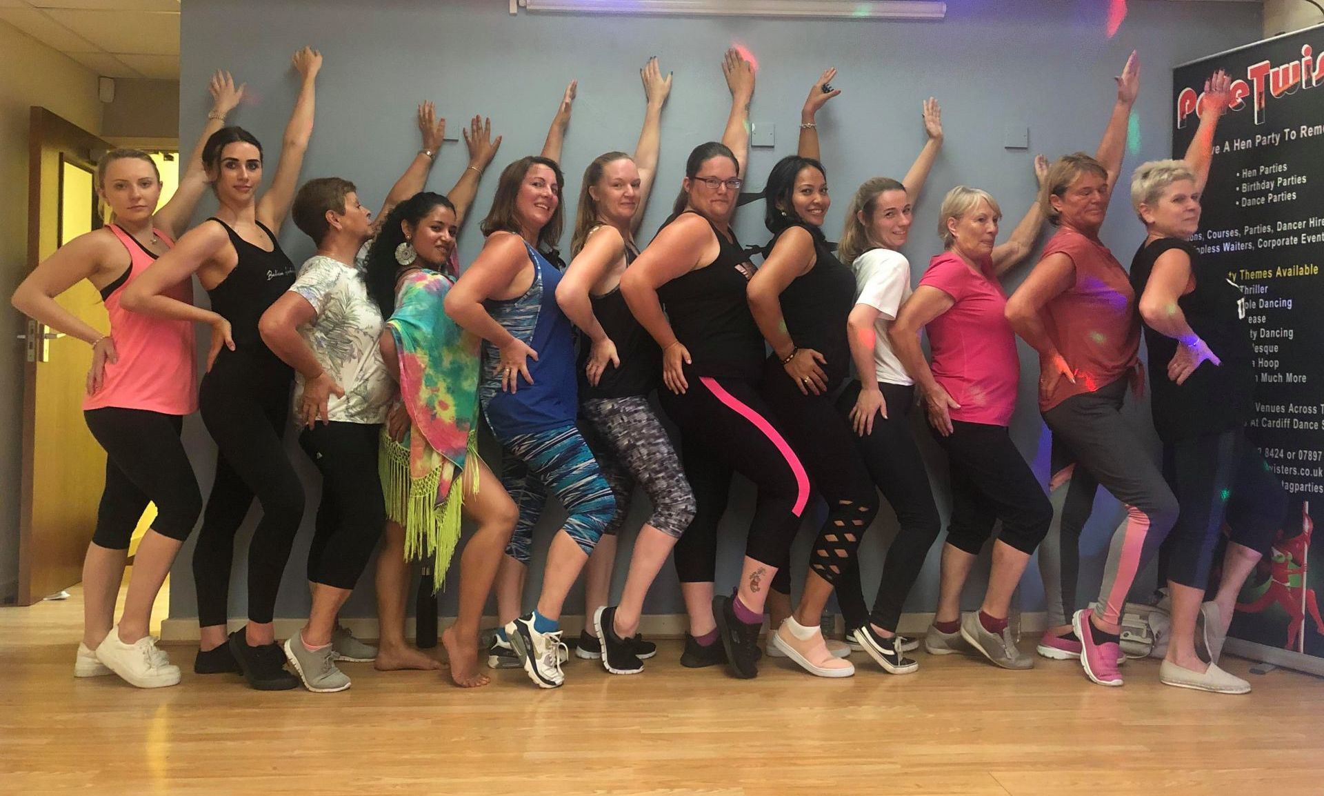 Group of women lined up dancing at a Bollywood themed hen party dance class, posing together in a colourful studio setting