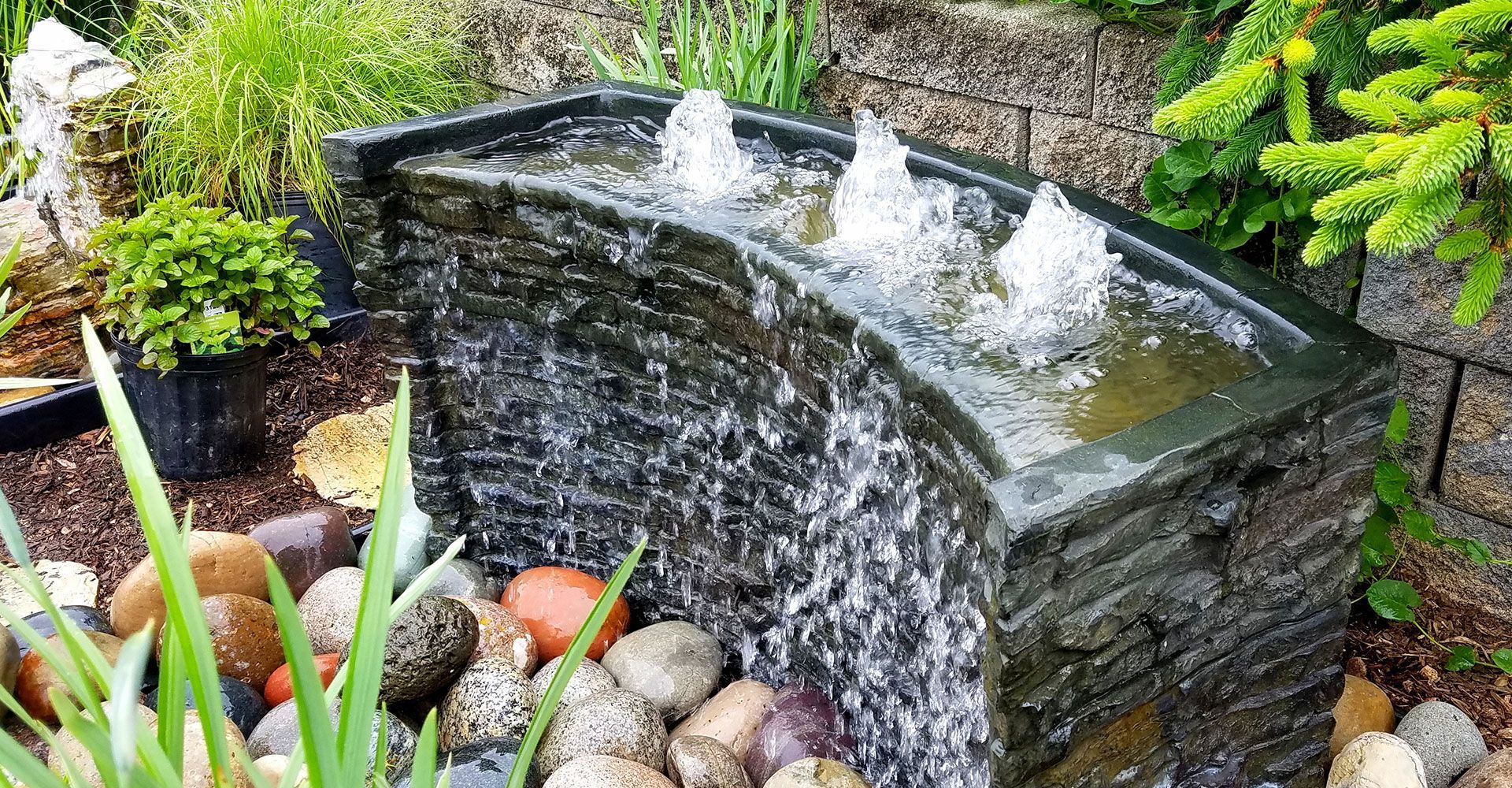 A water fountain is surrounded by rocks and plants in a garden.