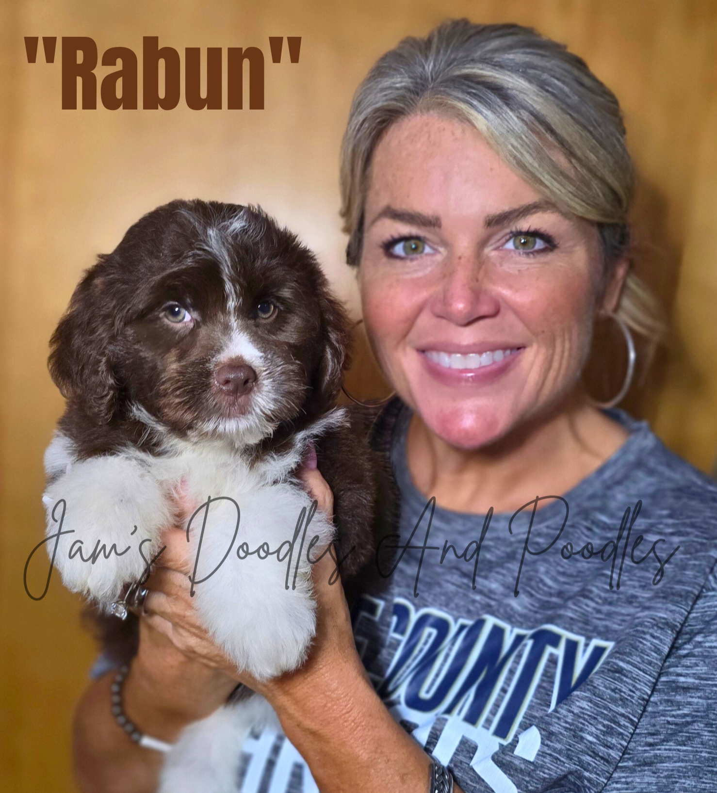 Woman holding a brown and white puppy named "Rabun." Both smile at the camera; a wooden background.