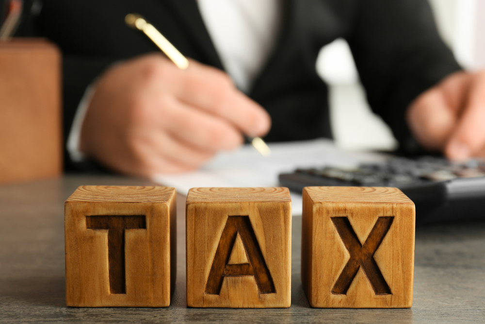 A man is writing on a piece of paper next to wooden blocks that say tax.