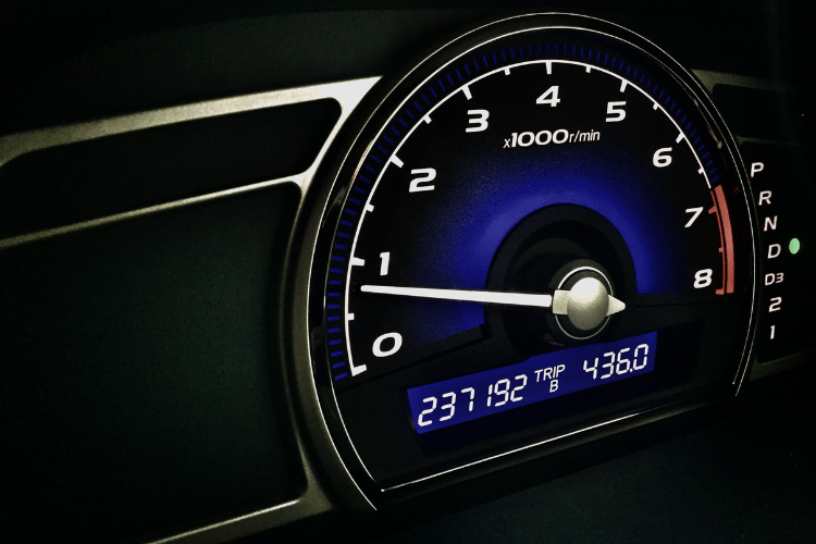 Car dashboard with illuminated tachometer and digital odometer display at night