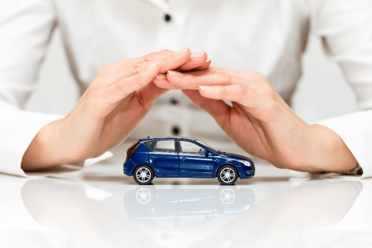 Hands protecting a blue toy car on a white surface